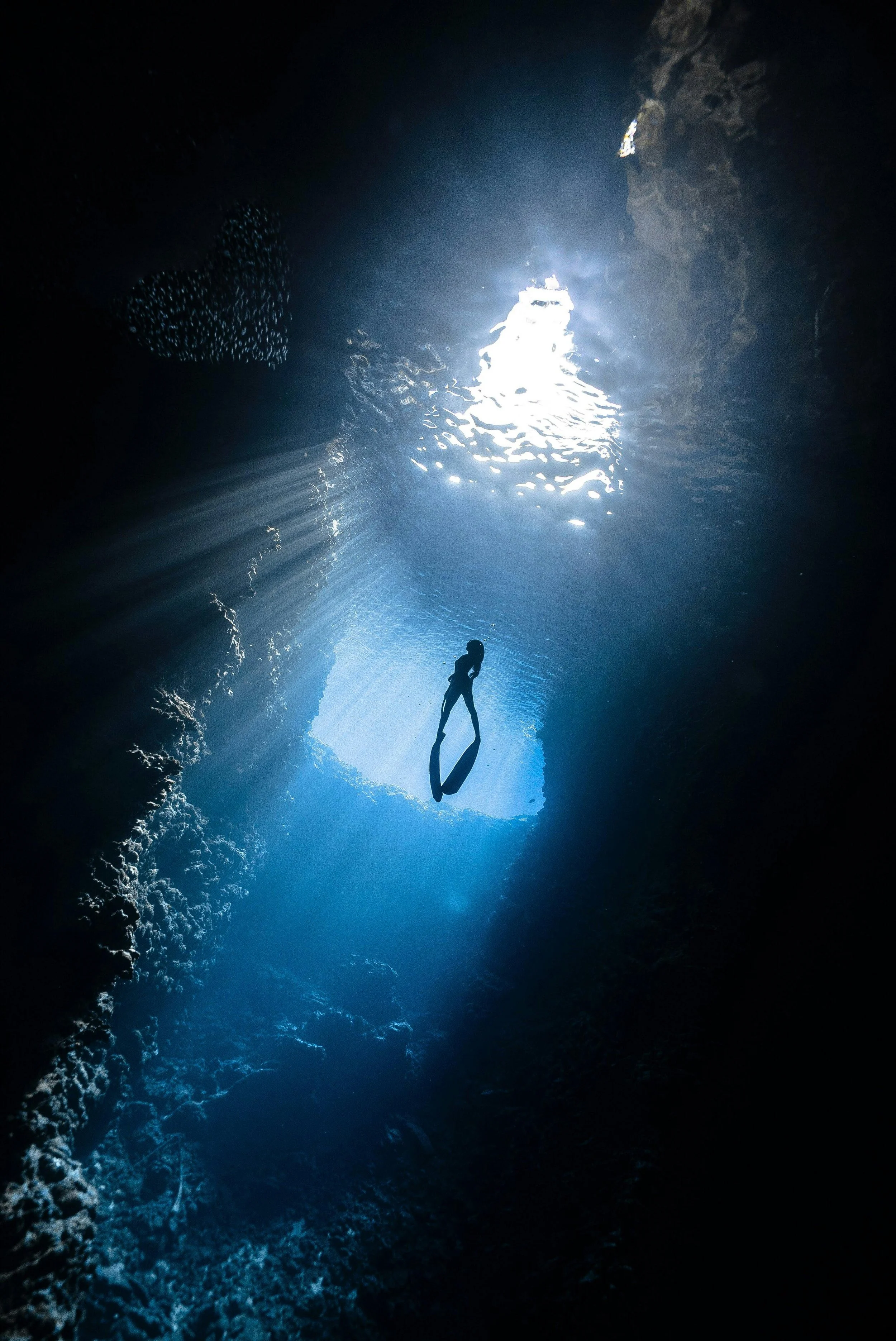 An underwater scene showing a scuba diver exploring a cave with sunlight streaming through an opening above.