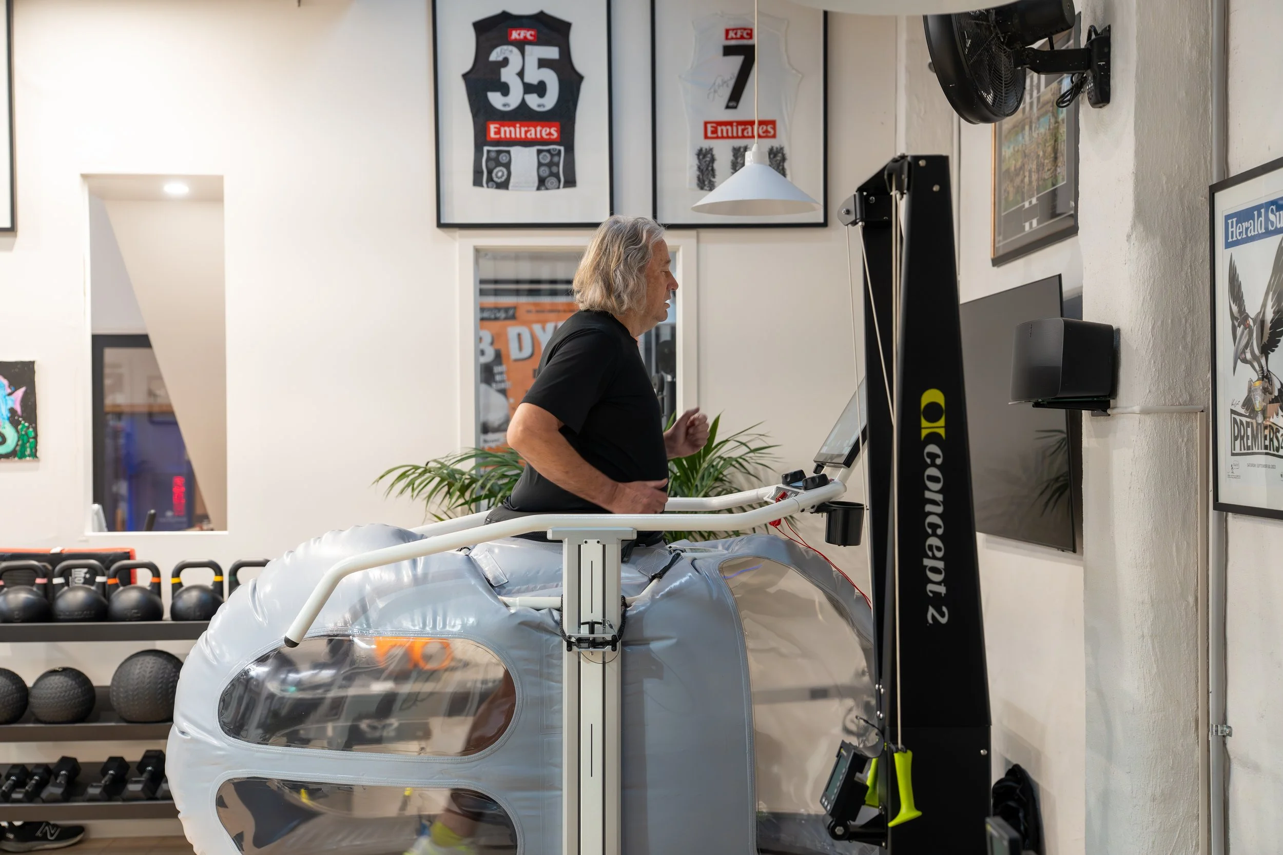 A man using a Treadmill inside a gym with memorabilia and framed sports jerseys on the wall.