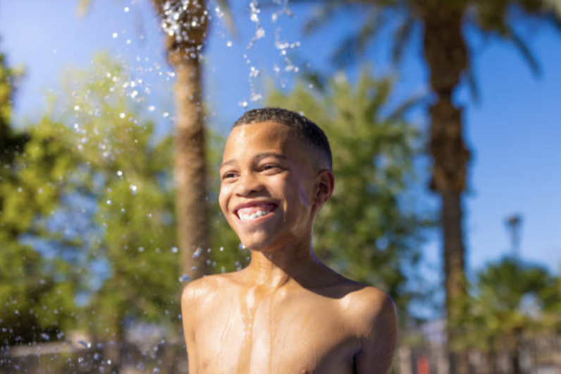 Smiling boy enjoying water splashes under palm trees on a sunny day.