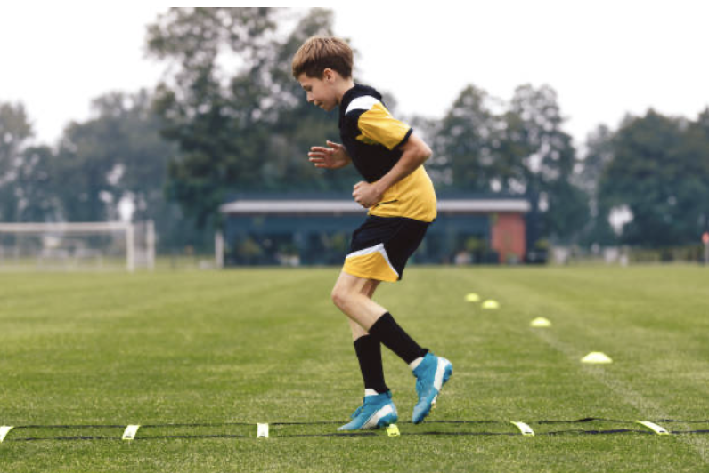 Young soccer player doing agility drills on a field.