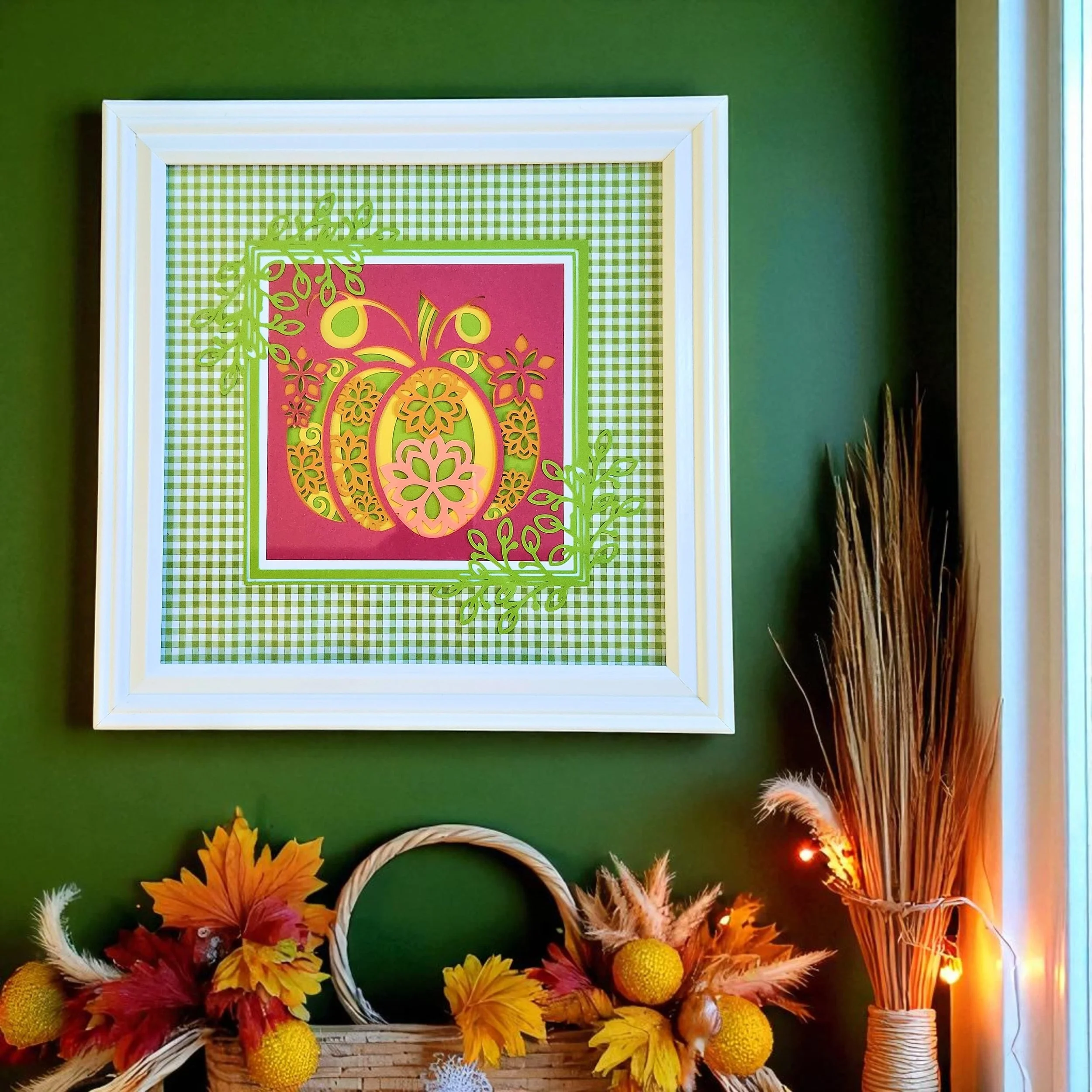 Framed 3D layered papercut pumpkin artwork with 8 colorful cardstock layers in red, yellow, green, orange, white, and plaid, displayed in a white 11x11 inch frame with glass cover and sawtooth hanger.