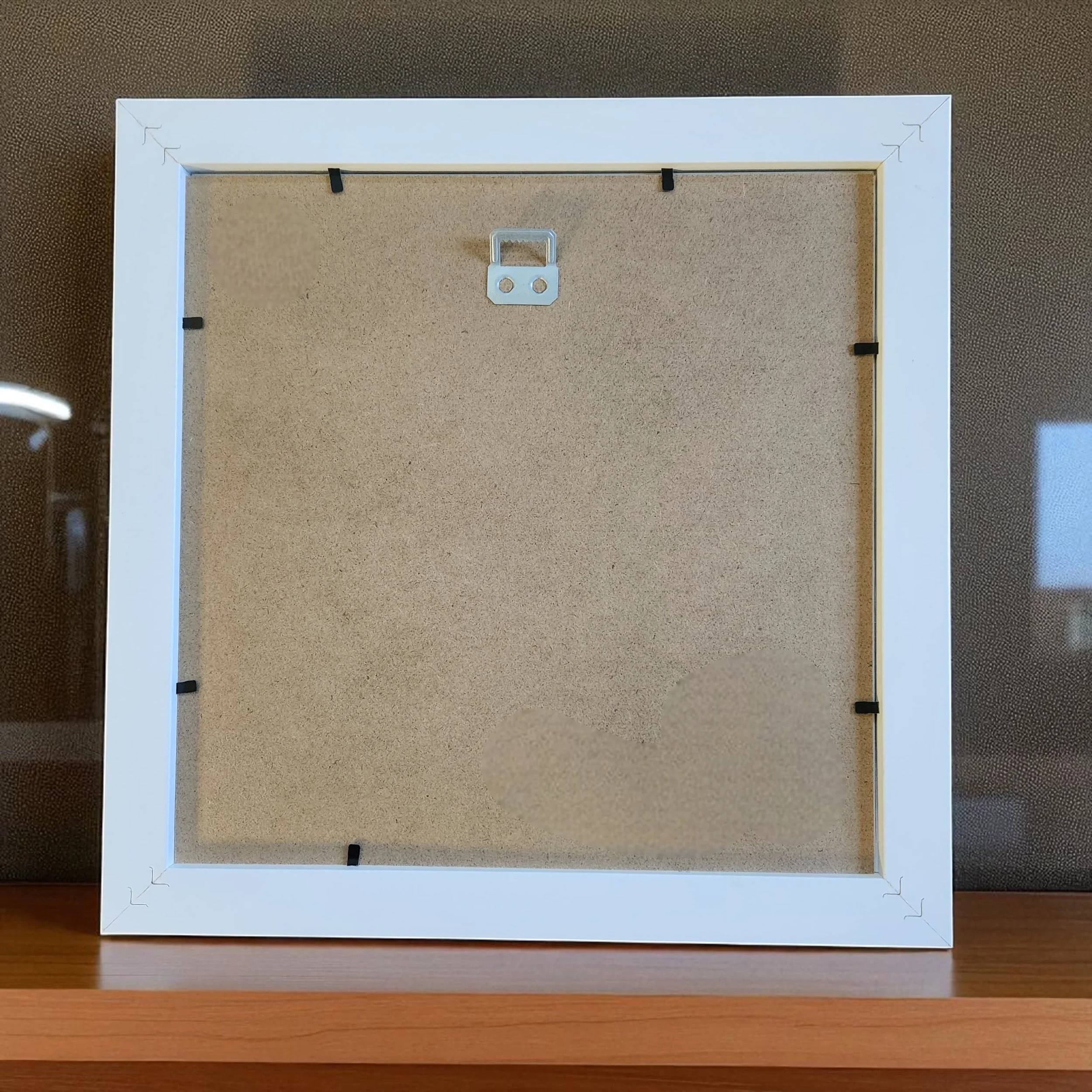Rear view of white 11x11 inch frame showing sawtooth hanger for easy wall mounting, backing board securely holding layered papercut pumpkin design.