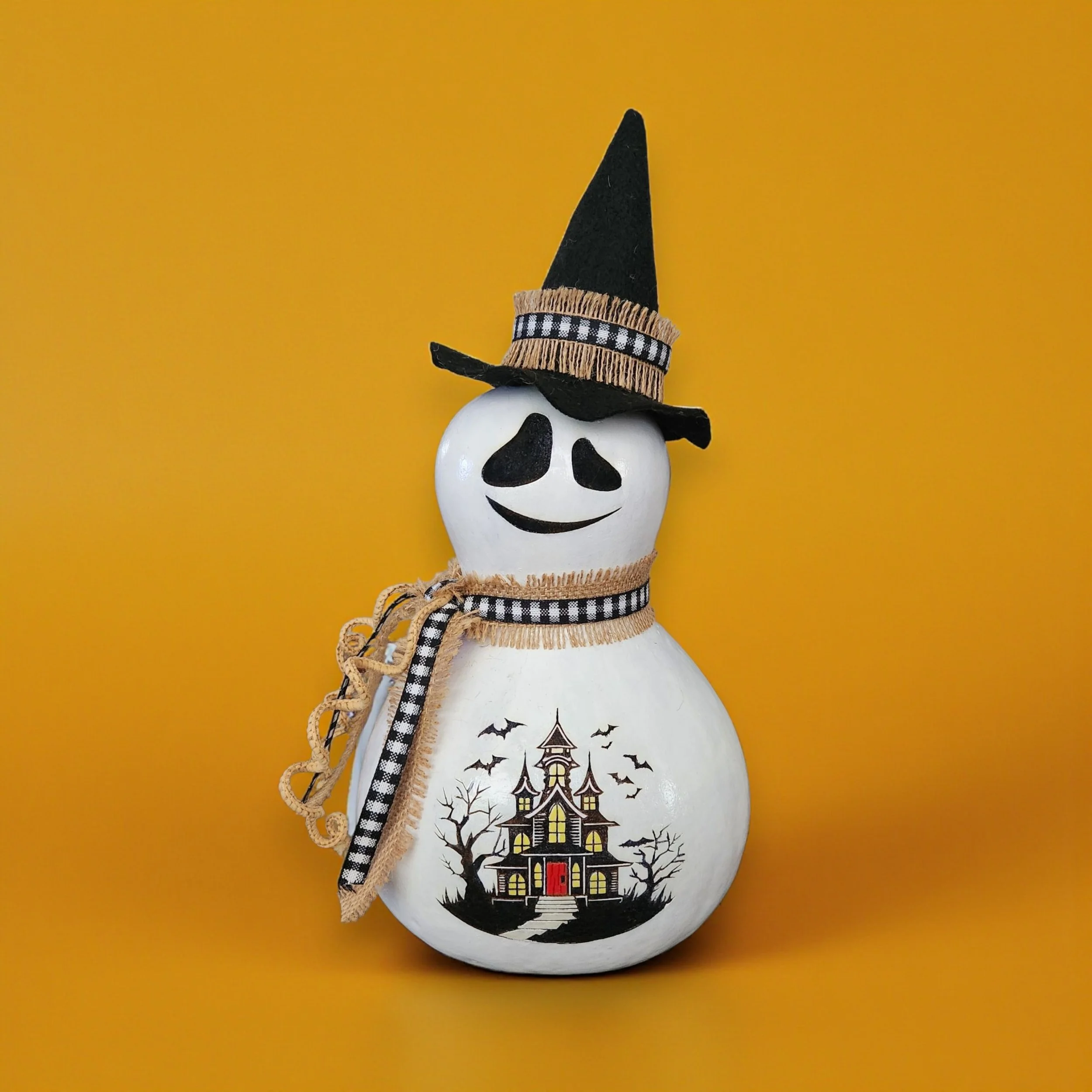 Front view of Ghost Witch Bottle Gourd with felt hat and rustic ribbon around its neck and spooky laser engraved and painted house on belly.