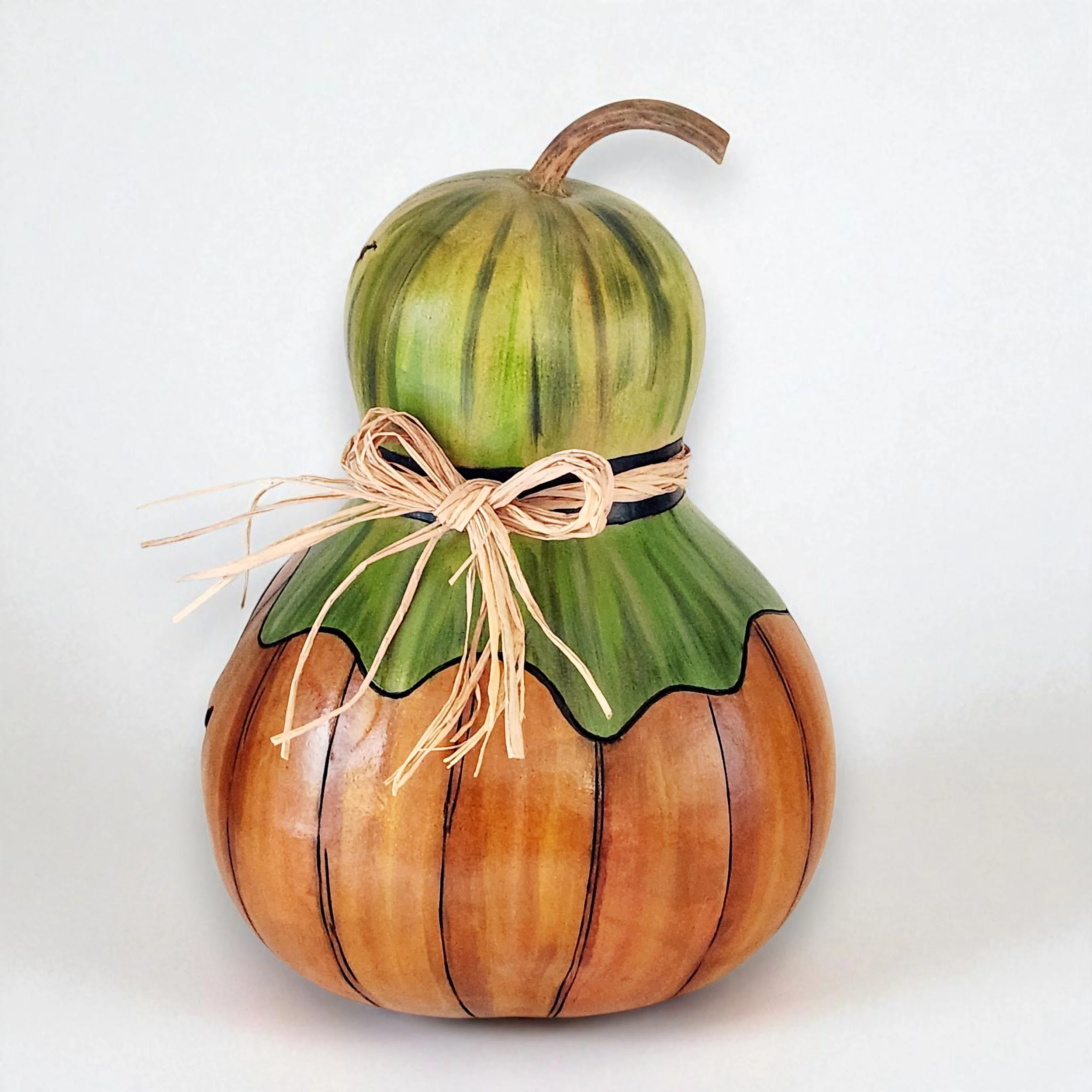Opposite side of the gourd lantern featuring a rustic raffia bow tied near the top. The leafy green hat adds texture and seasonal charm.