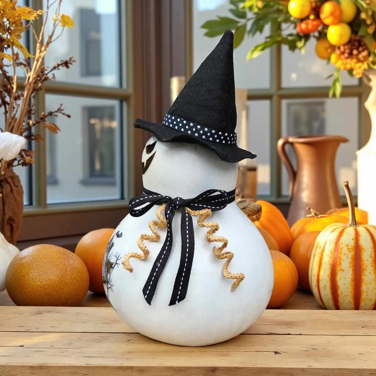 Close-up of black felt witch hat and shimmering ribbon trio on neck of laser-engraved ghost gourd.