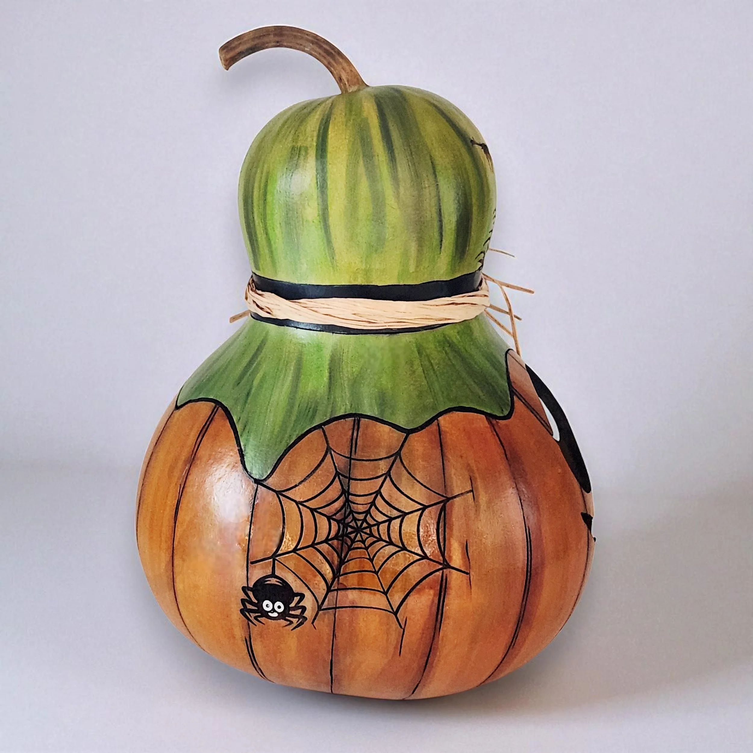 Side view of the gourd lantern showing a tiny spider nestled in a laser-engraved web design. The curved surface of the gourd highlights the engraving and wood burned detail.