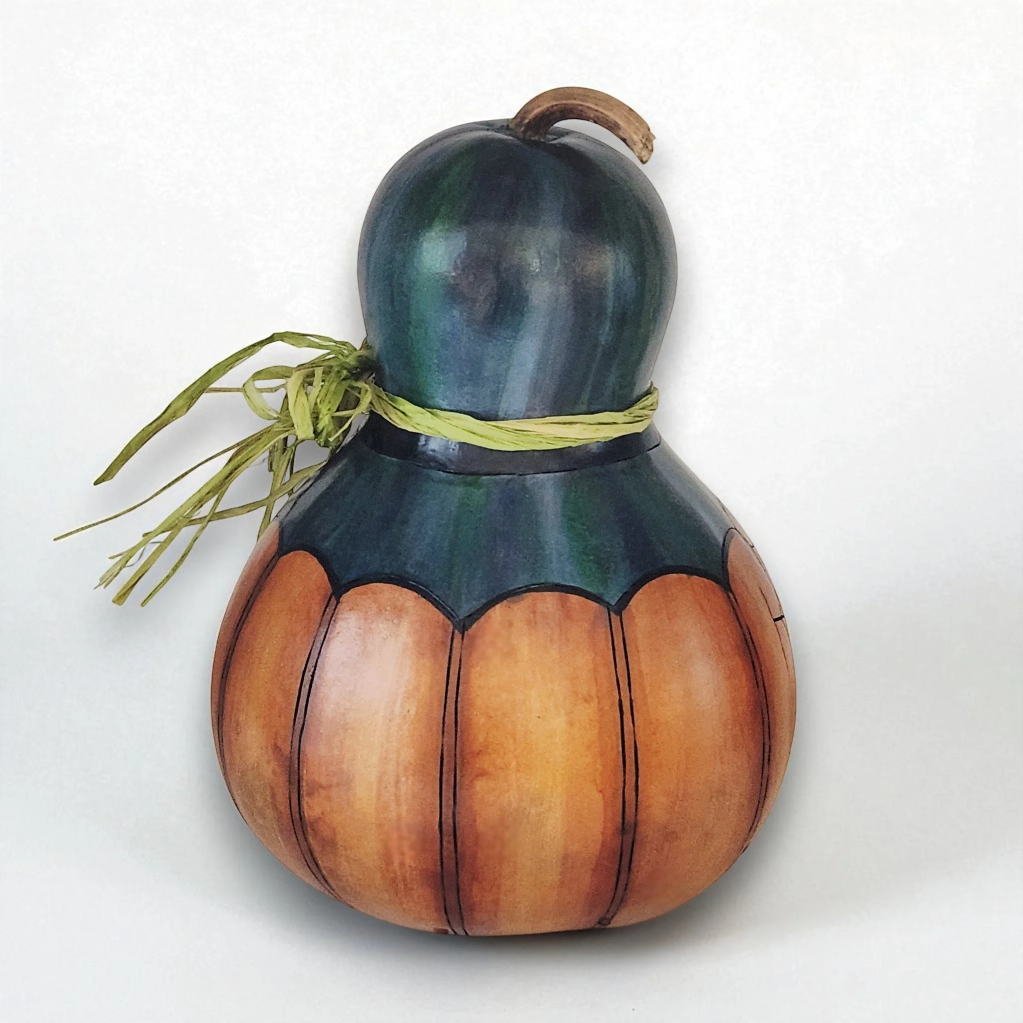 Back view of bottle gourd jack-o-lantern showing wood burned details, raffia bow and green colorful hat.