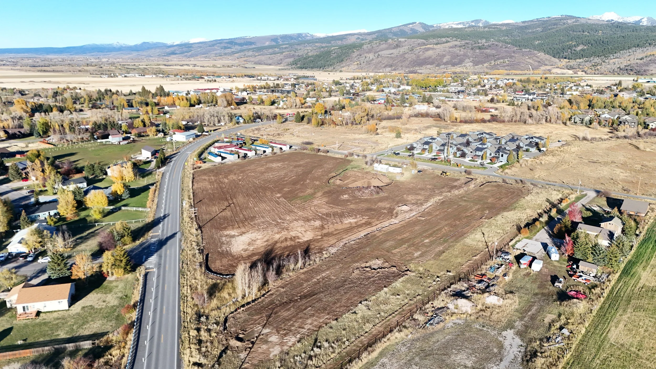 An aerial view of a construction site with a small building, piles of dirt, construction vehicles, and a cleared area for future construction.