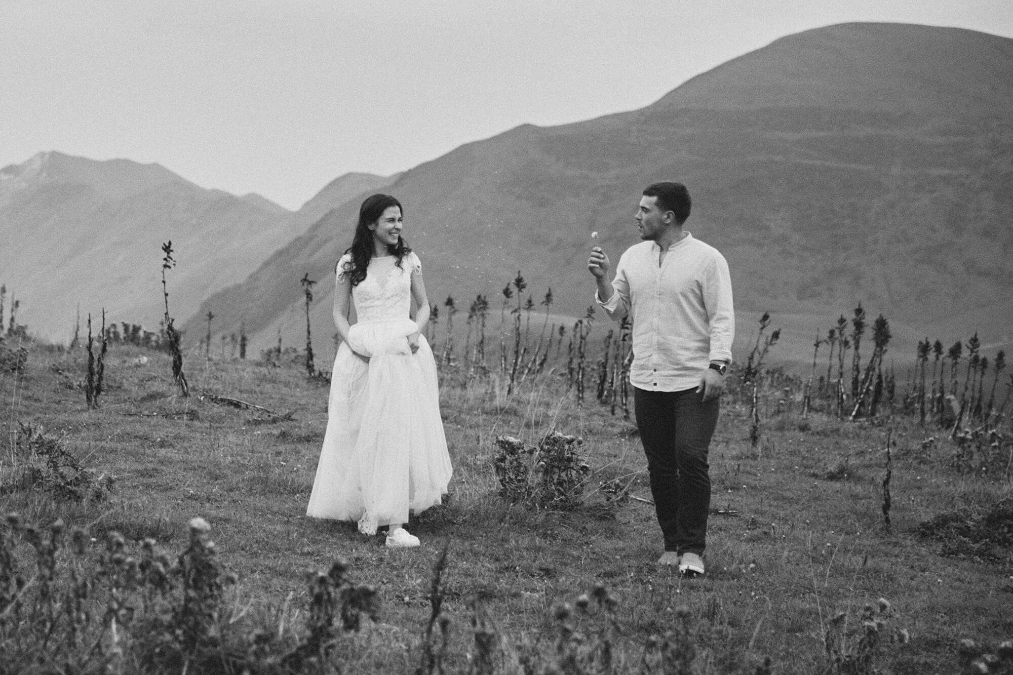 Romantic engagement photo: groom blowing dandelion seeds at bride in the mountains