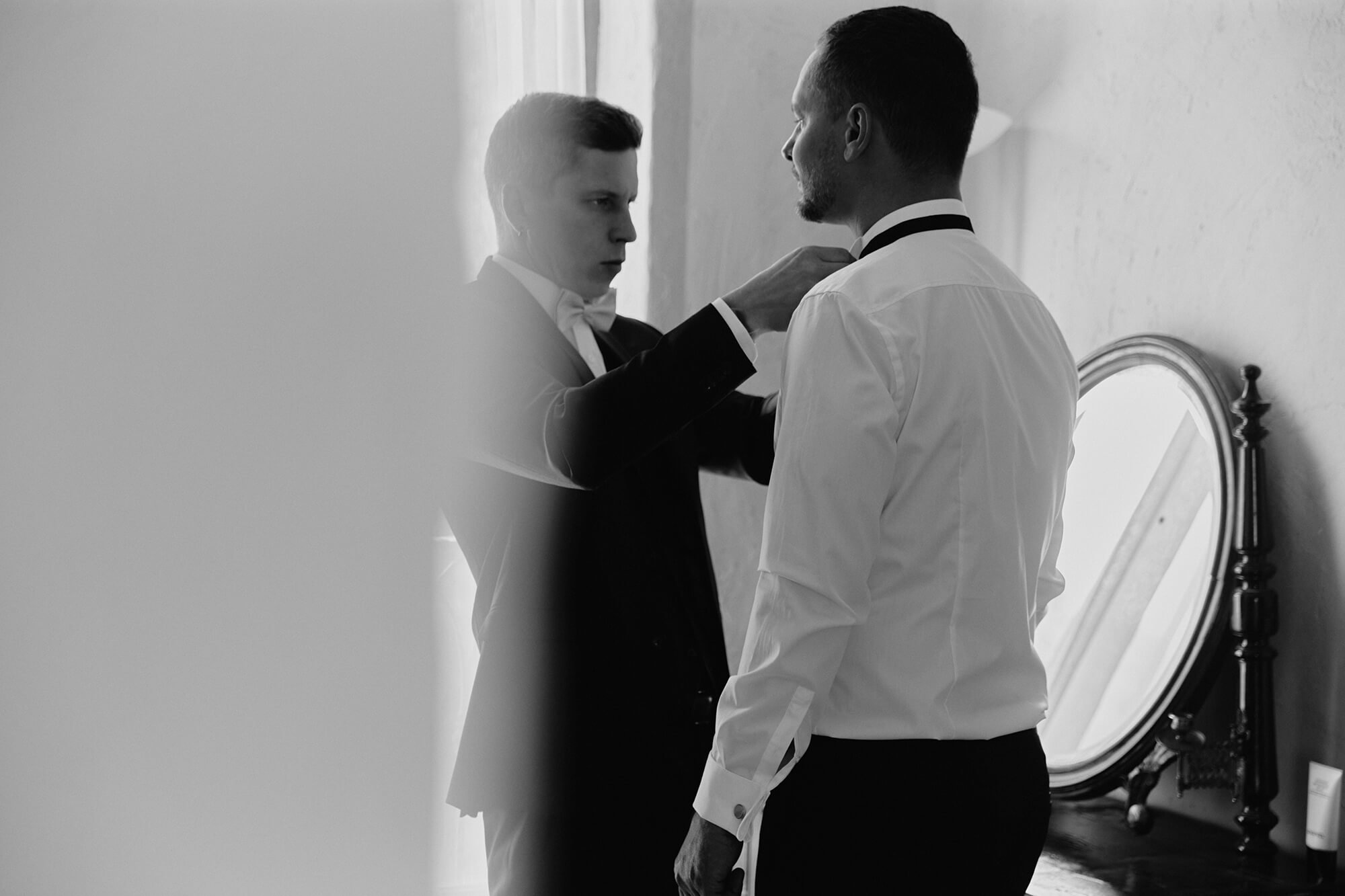 Groom getting ready as best man adjusts his collar