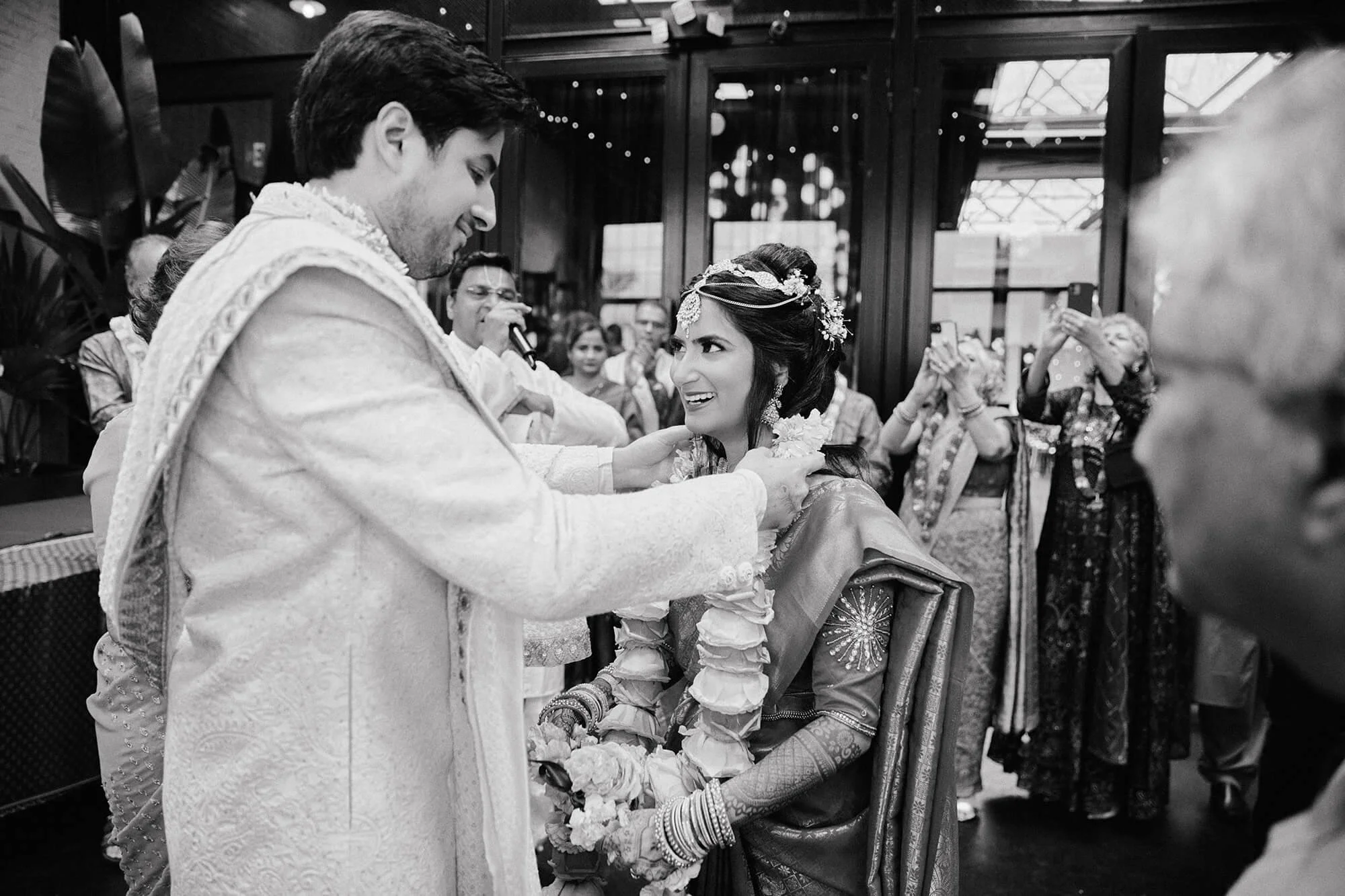 Black and white photo of the groom placing a wedding garland on the bride.