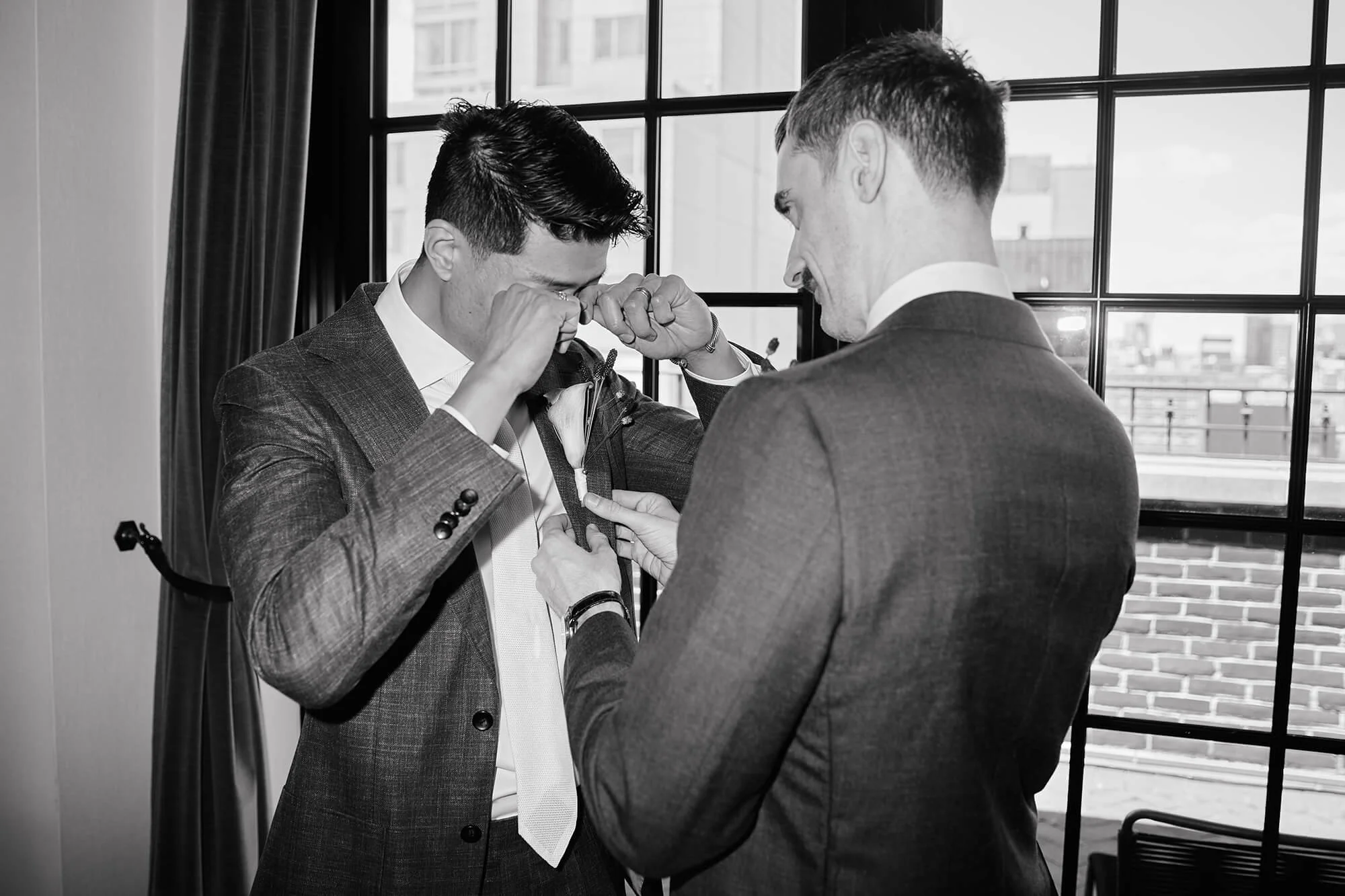 Emotional moment: groom crying as partner adjusts boutonniere