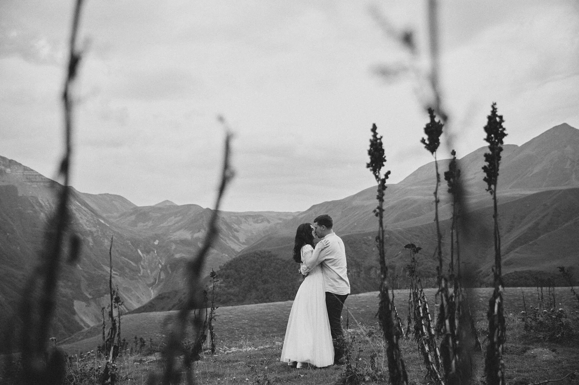 Romantic engagement moment: couple kissing surrounded by mountains