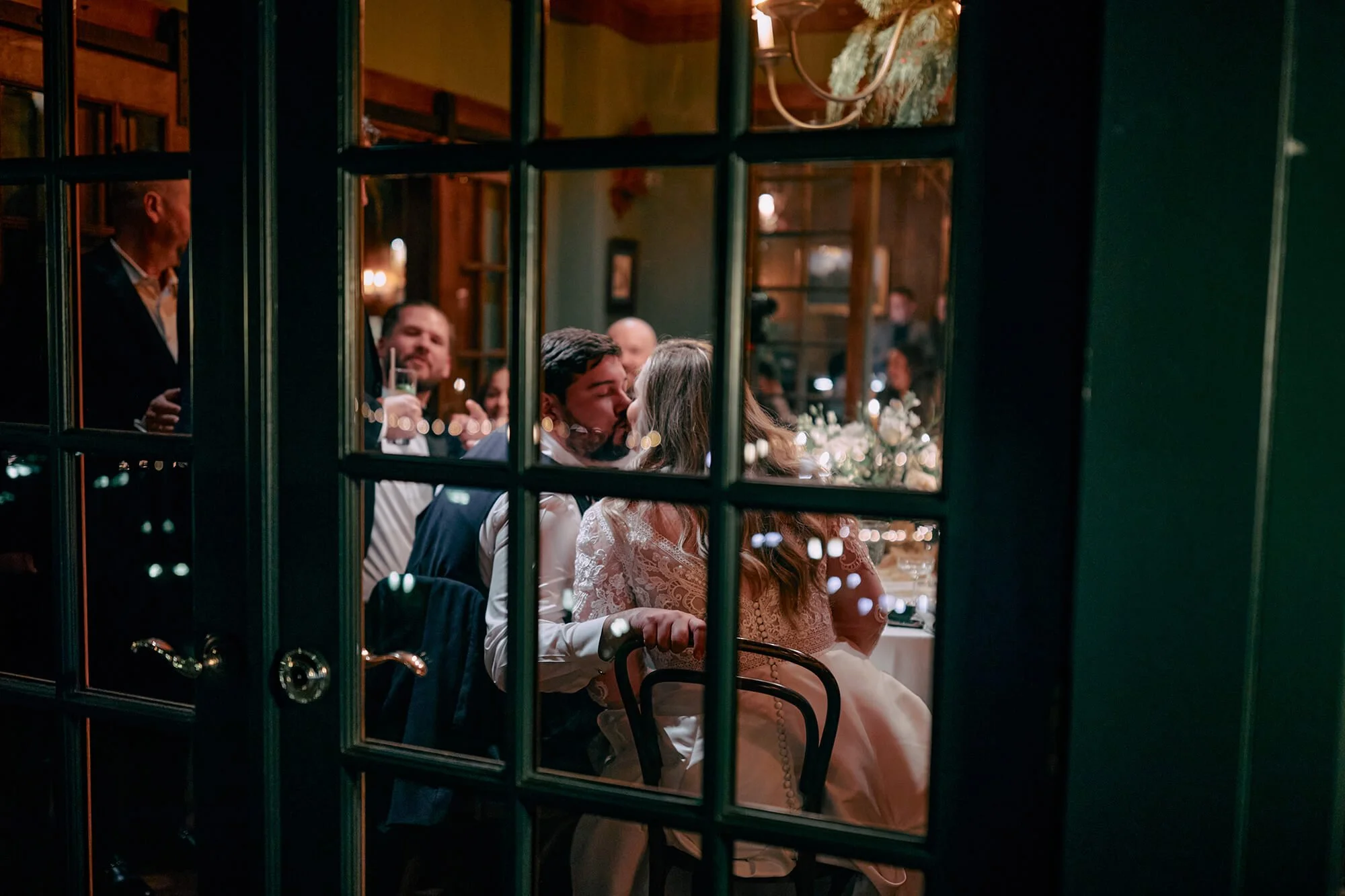 Through-the-window shot of dinner reception, cozy and candid