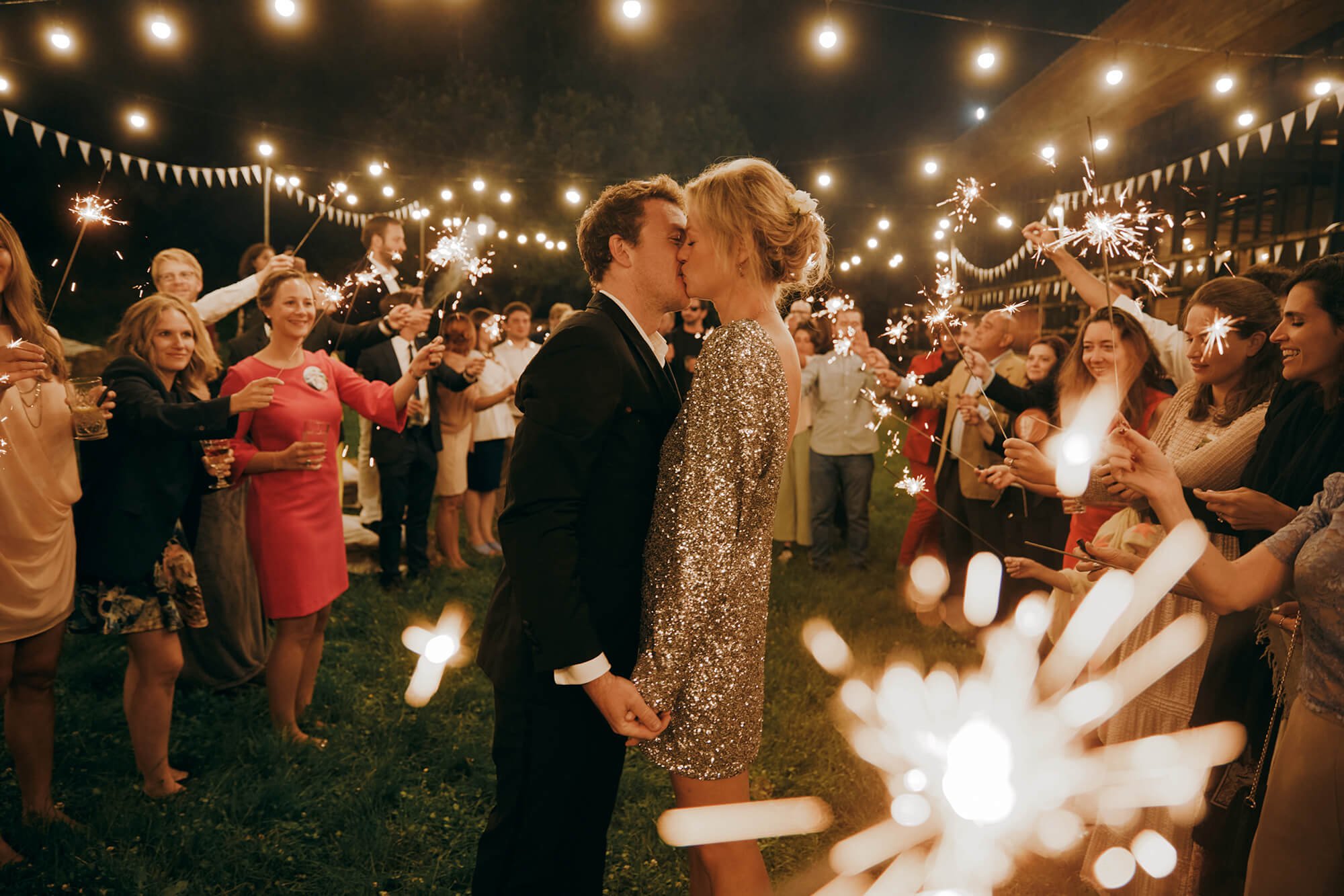 Couple kissing under sparklers and guests laughing during sparkler exit
