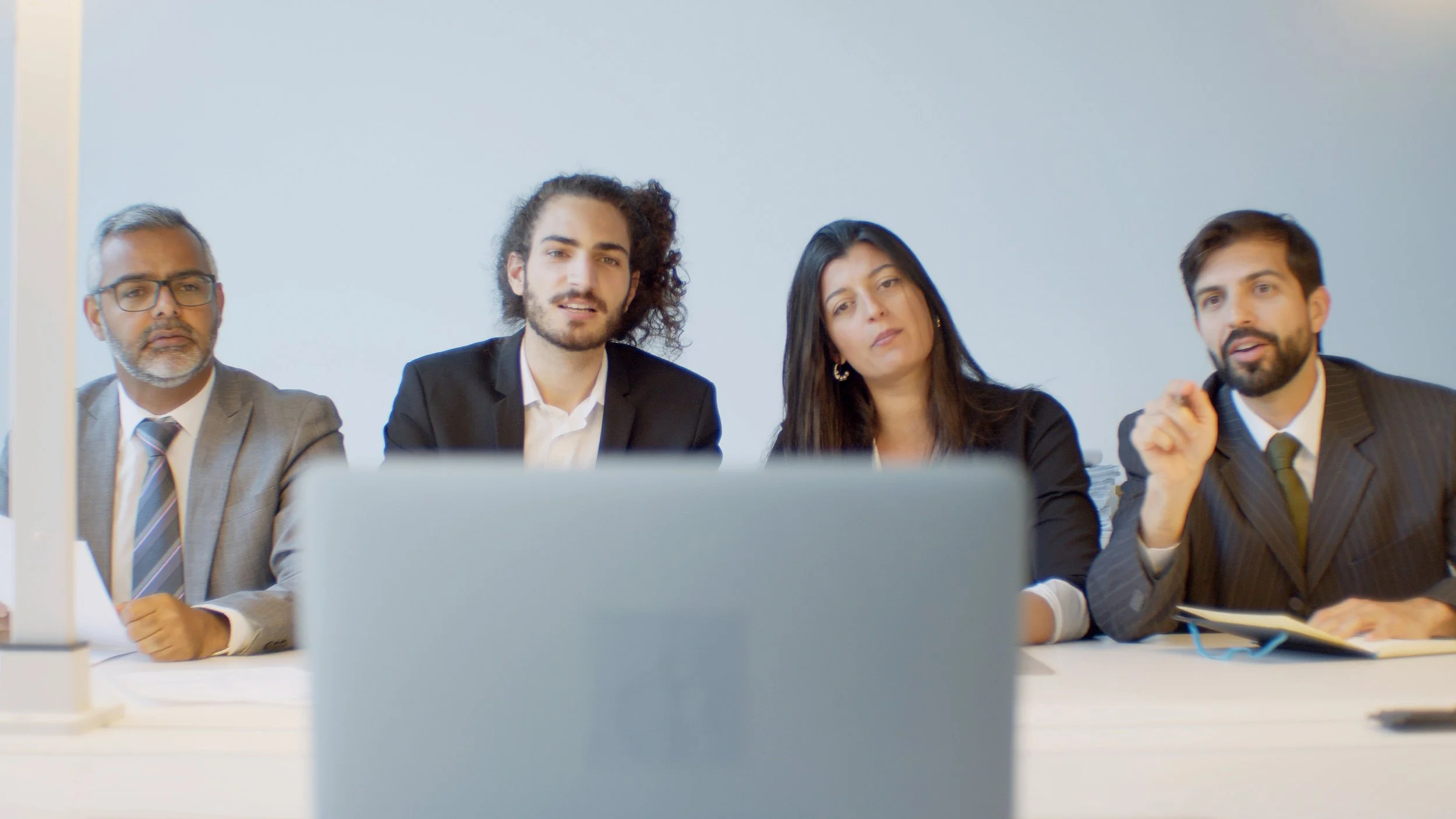 Four professionals attending a virtual meeting or presentation in an office setting, sitting at a table.
