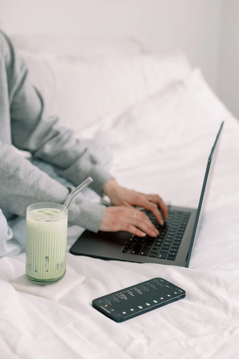 Woman sitting with a laptop and a green health smoothie, ready to connect and offer caring naturopathic support