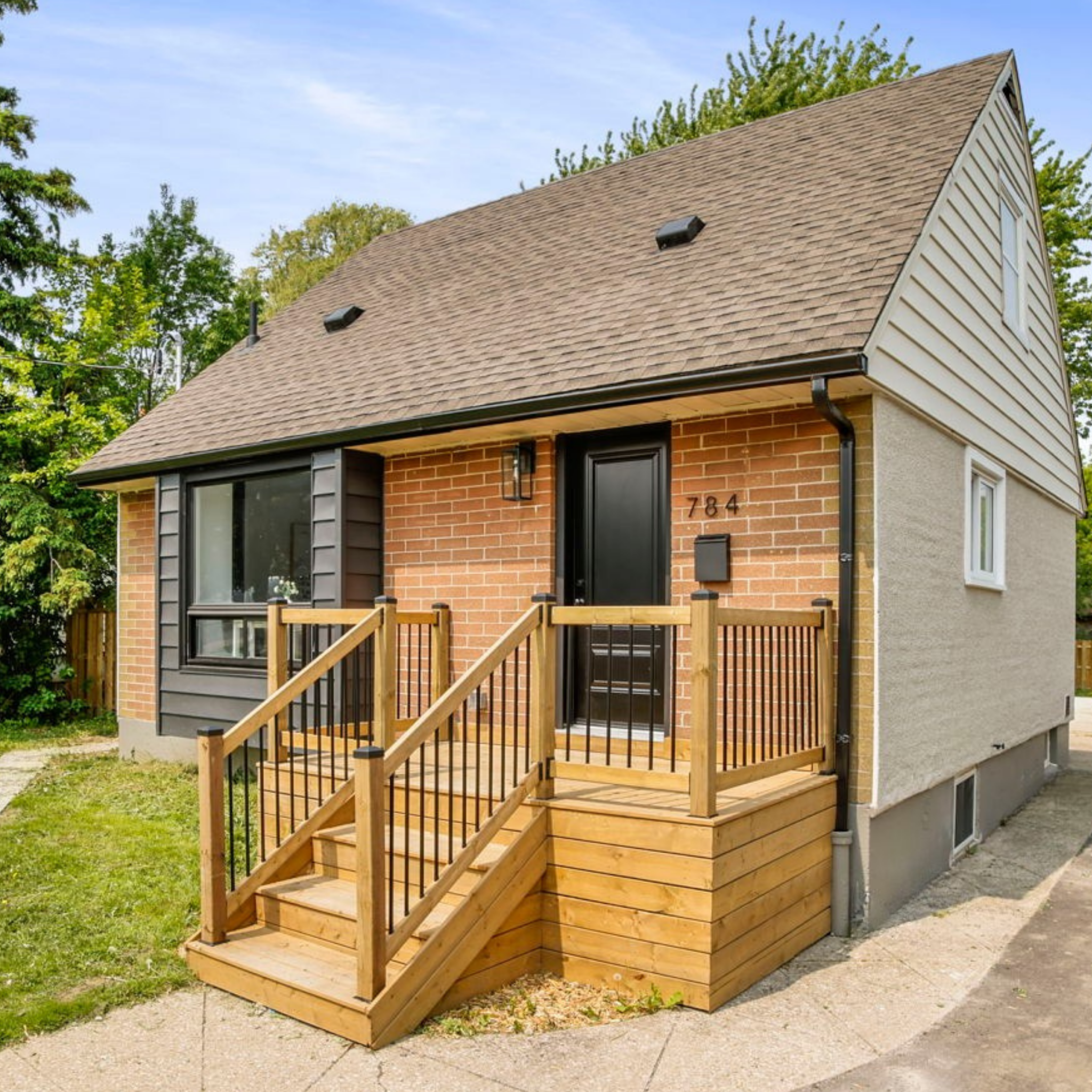 Front view of a house with brick and siding exterior, new wooden stairs leading to the black front door, and a small porch with a railing. The house has a sloped roof with two vents and a small window on the side.