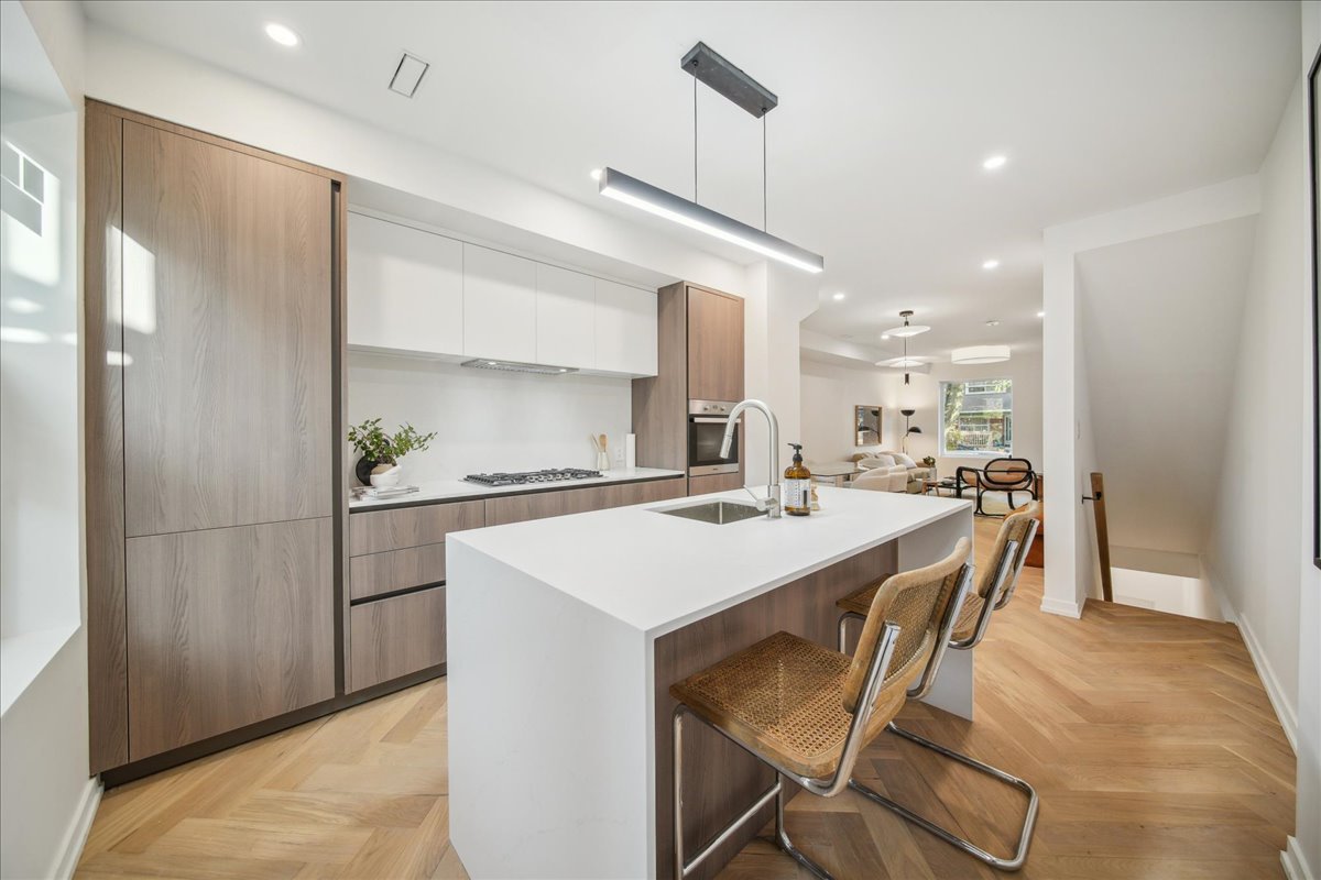Modern kitchen with wood cabinets, white countertop island, bar stools, and built-in appliances.
