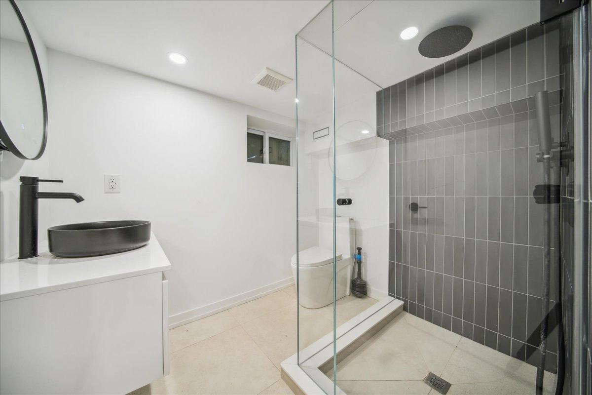 Modern bathroom with glass shower, black vessel sink, and large mirror