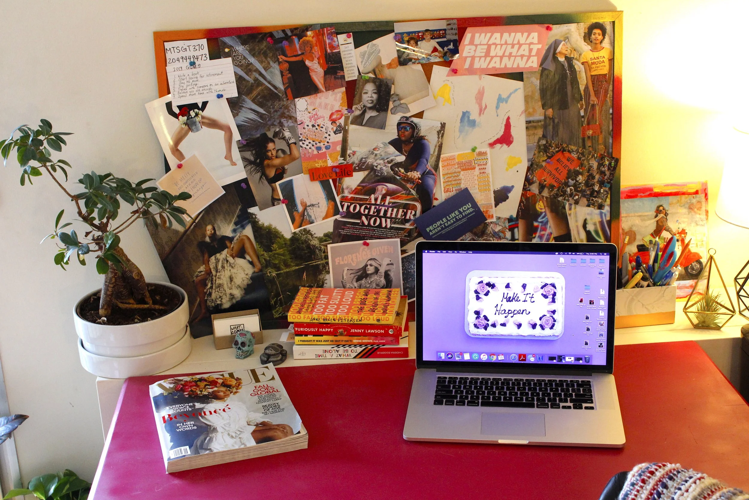 Colourful pink desk with a vision board behind it.