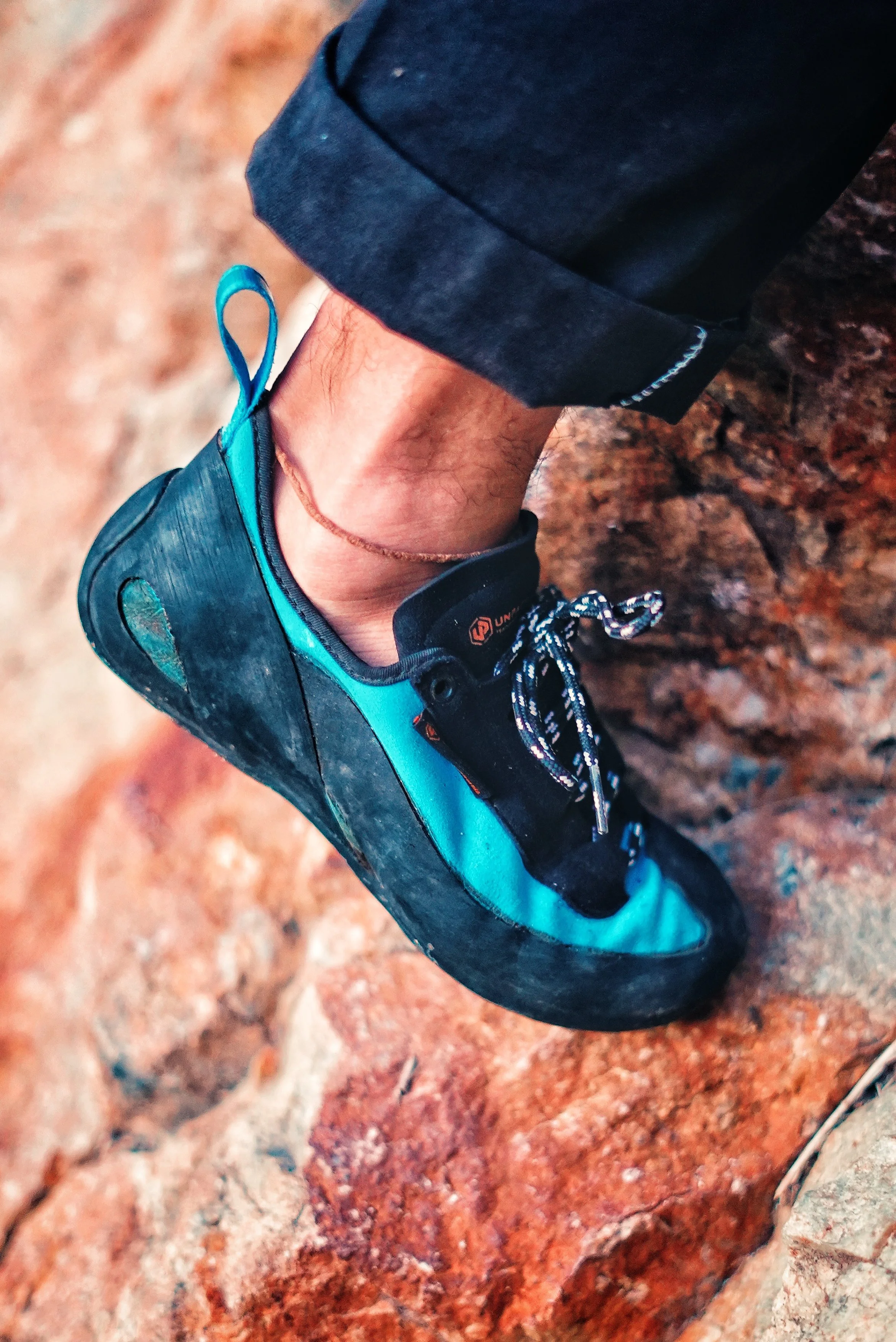 Close-up of a person's foot wearing a blue and black climbing shoe on a red rocky surface.