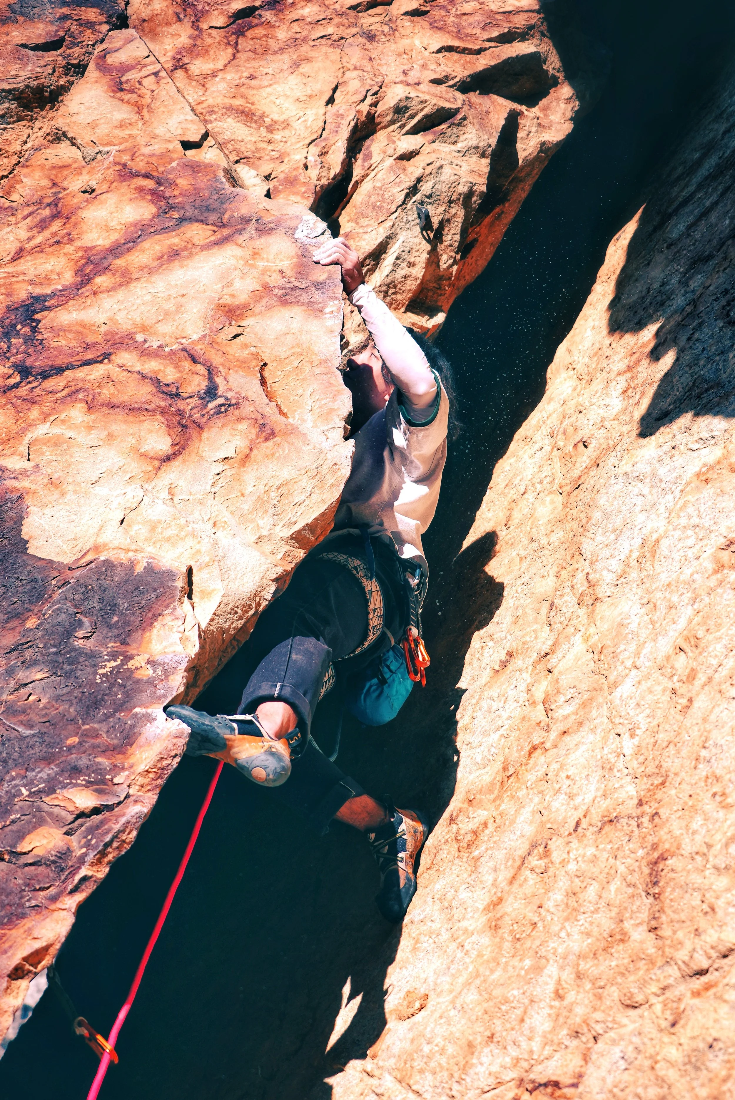 A person rock climbing between two large sandstone cliffs, wearing climbing gear and holding onto the rocks.