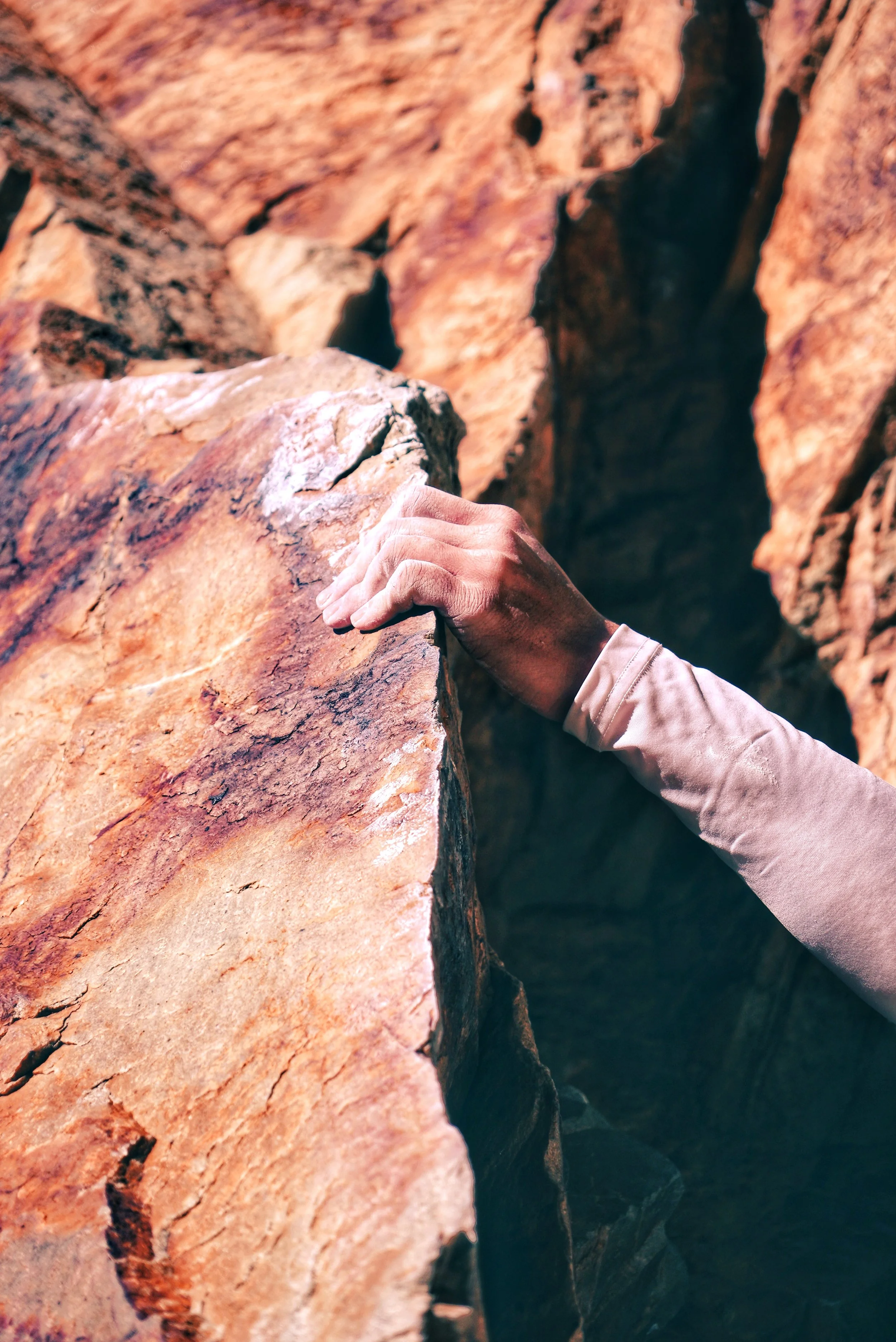 A climber's hand gripping a large rock in a canyon with orange and tan rock formations.