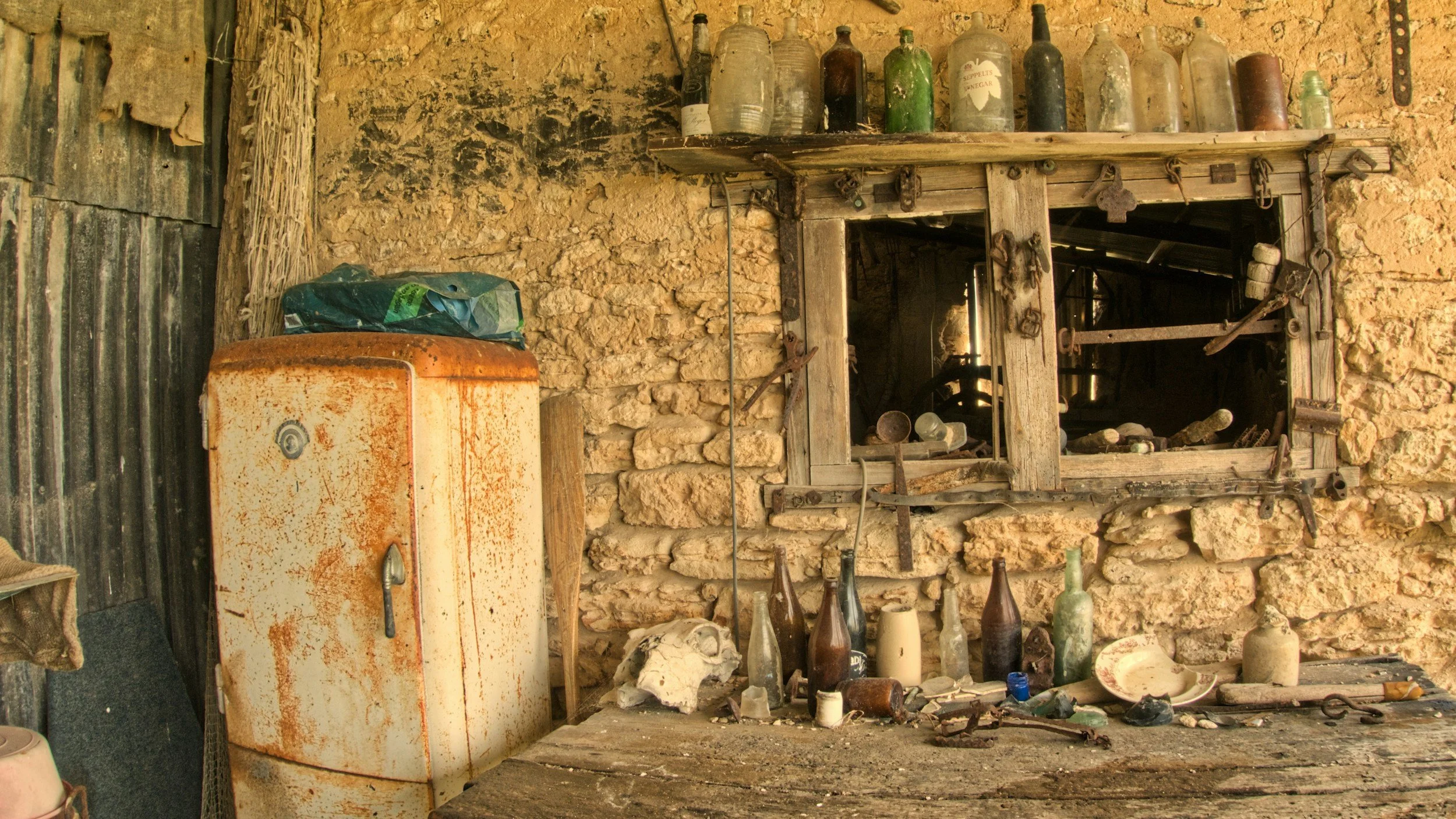 Rustic Greek shack, empty bottles, rusty fridge, stone walls, wooden table, About Pavlos Greek Busselton