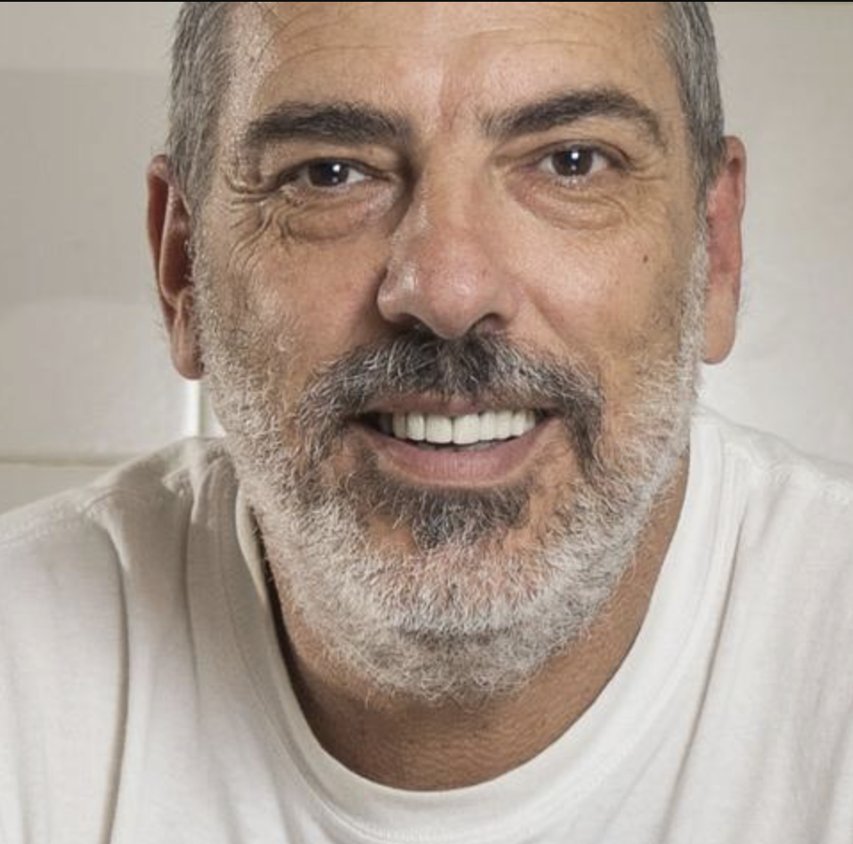 Close-up of a middle-aged man with gray hair and beard, smiling and wearing a white shirt.