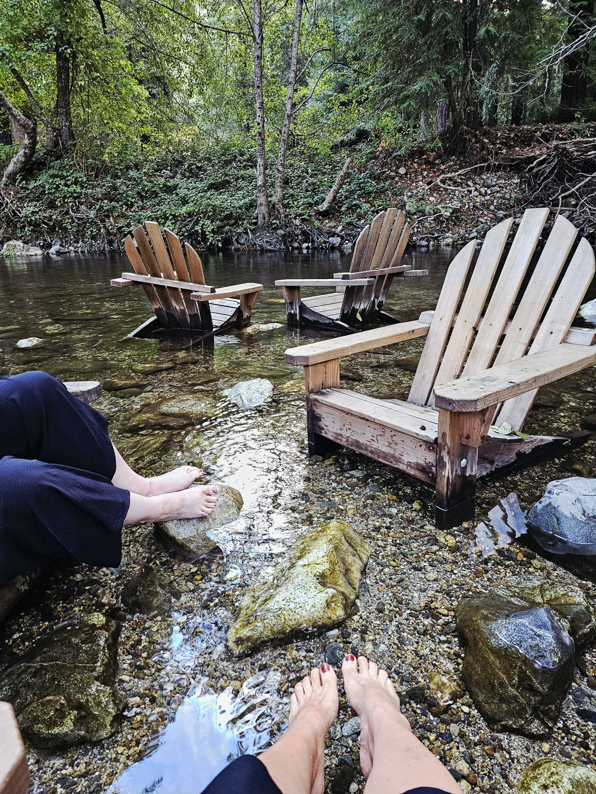 Nestled beneath towering redwoods, this peaceful creekside escape in Big Sur invites you to slow down and reconnect. With our feet immersed in the cool, flowing water and Adirondack chairs resting gently in the stream, it became the perfect place.