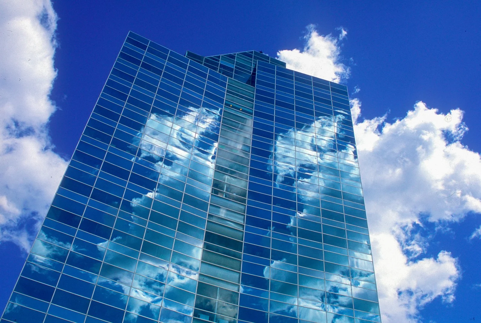 A modern glass skyscraper reflecting the blue sky and white clouds.