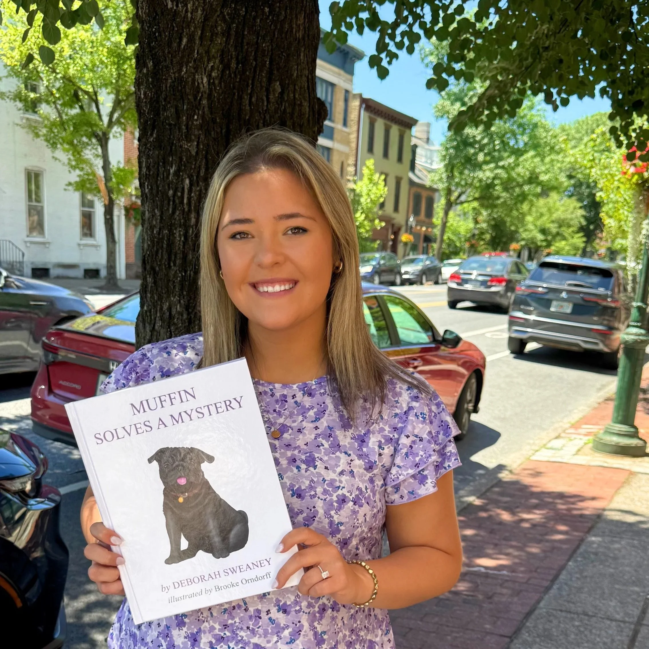 Brooke Orndorff holding a book titled 'Muffin Solves a Mystery' at the book release signing event at Whistlestop Bookshop.