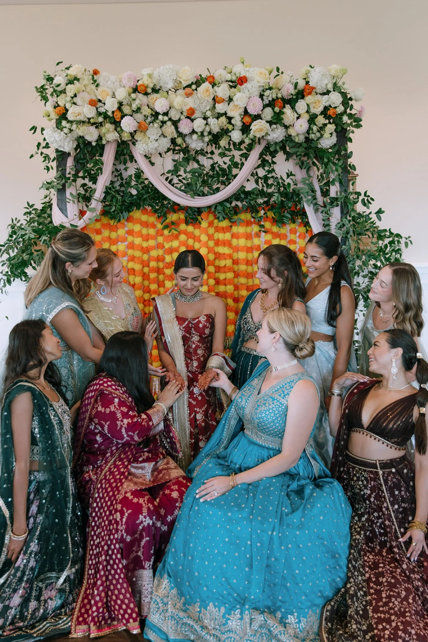 Indian bride and her bridesmaids in front of an orange and yellow floral backdrop