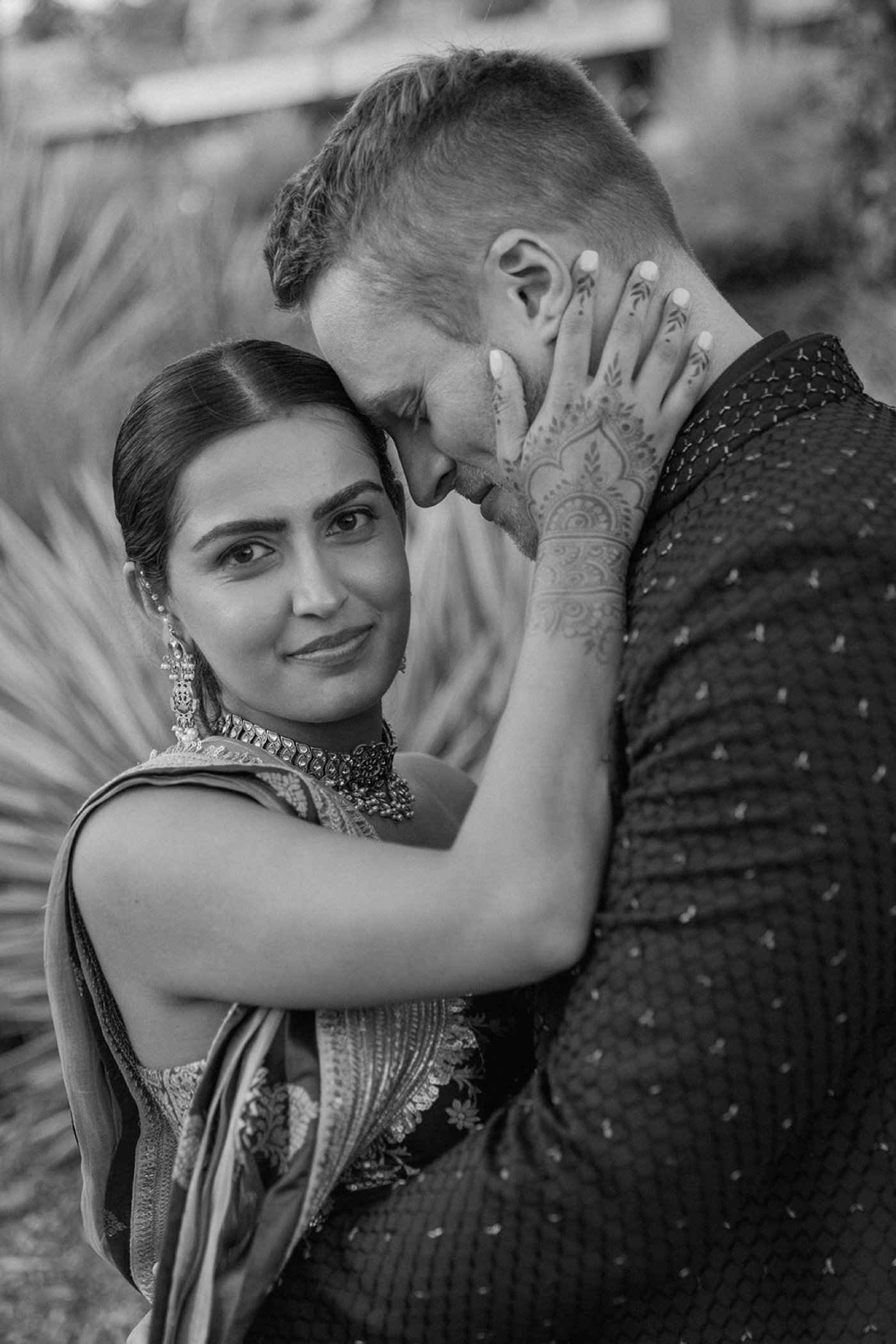 Black and white portrait of a bride holding her groom's face and looking at the camera
