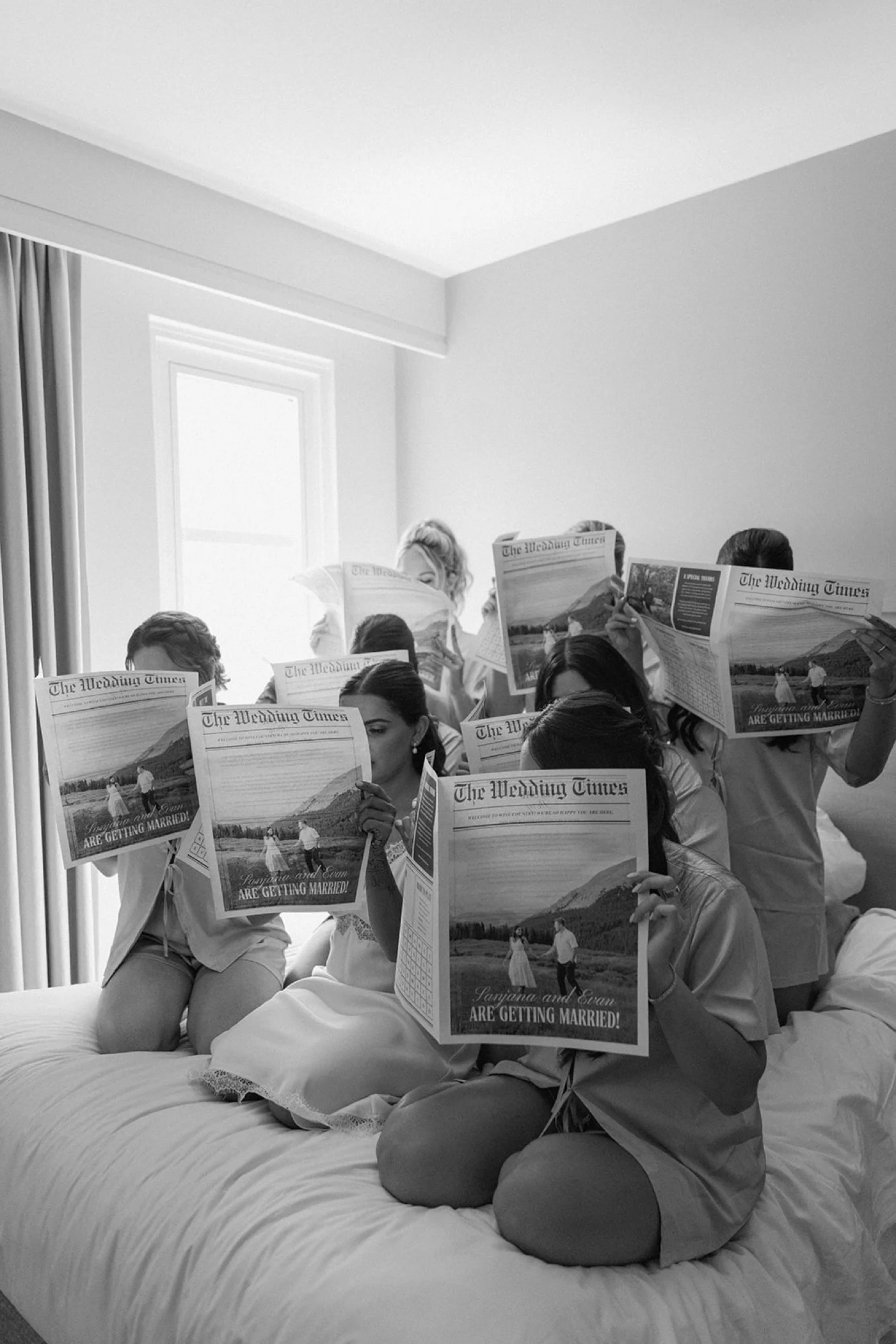 Bride and her bridesmaids reading custom wedding newspapers on a bed