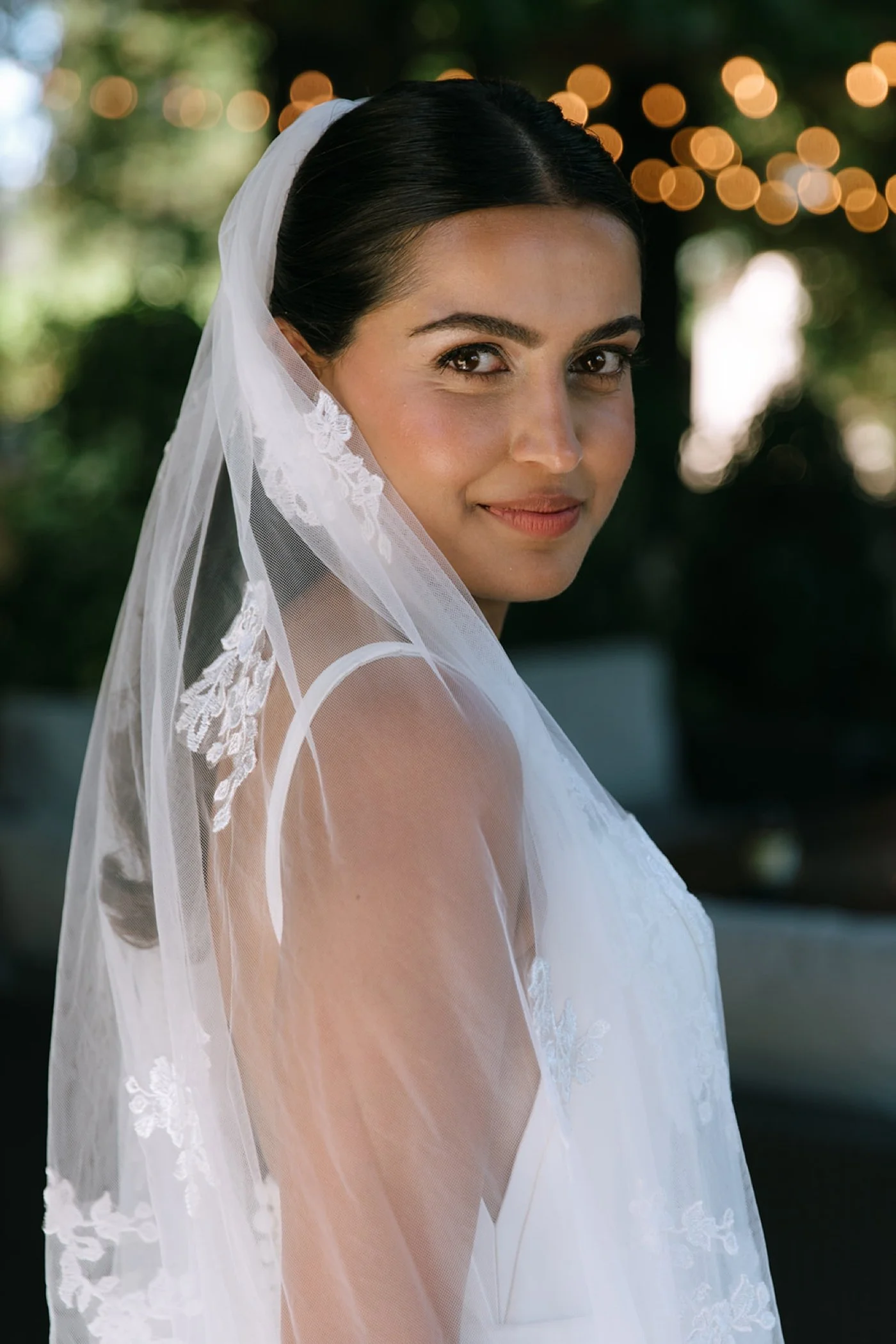 Bride wearing a floral lace veil and looking over her shoulder at the camera