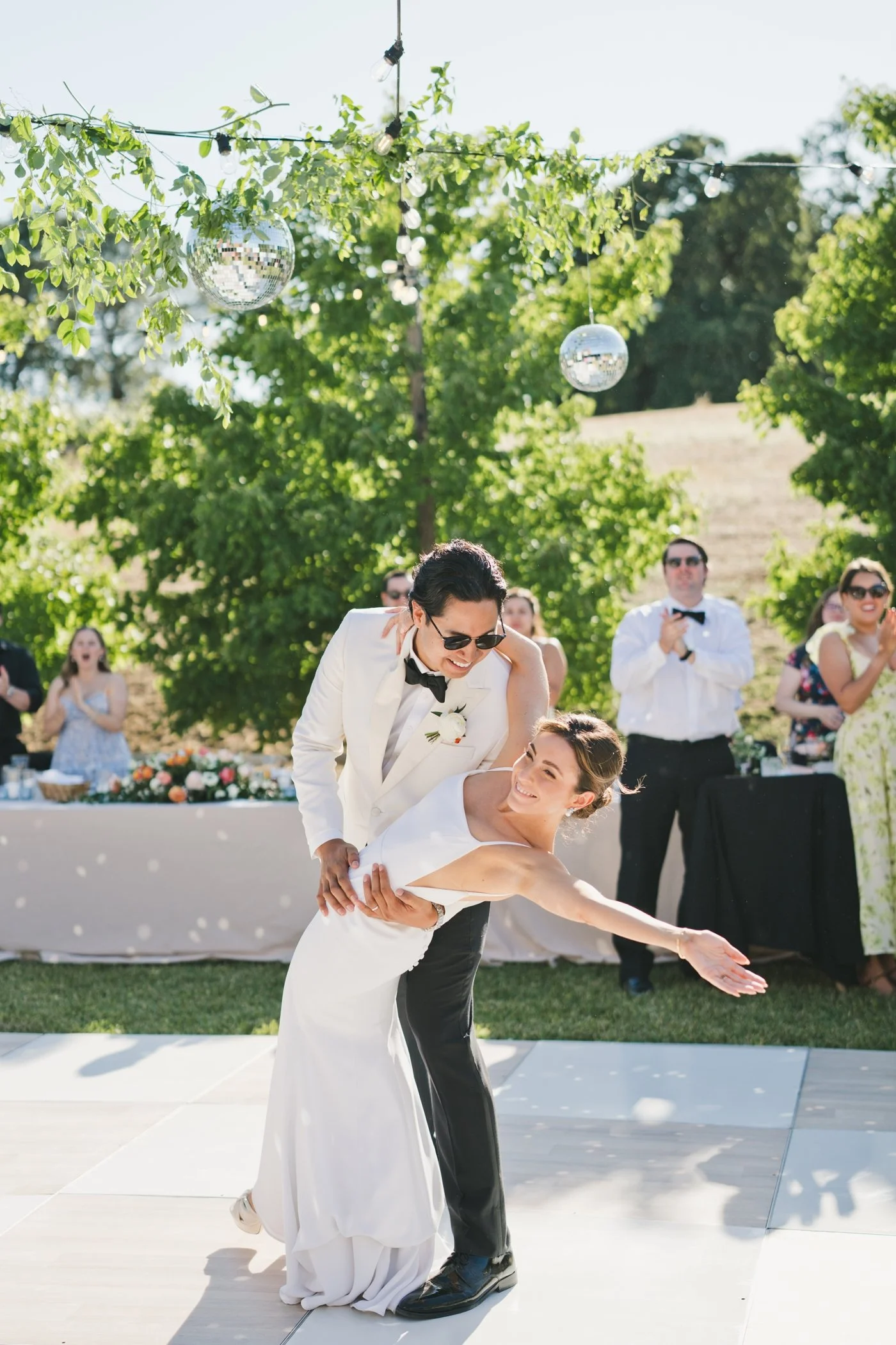 Groom dipping his bride as she waves to their wedding guests