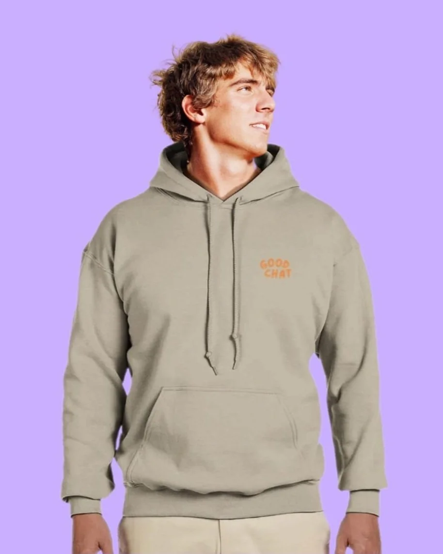 A young man with curly hair looking to the right, wearing a light-colored hoodie with orange text that says 'GOOD CHAT' on the chest, standing against a purple background.