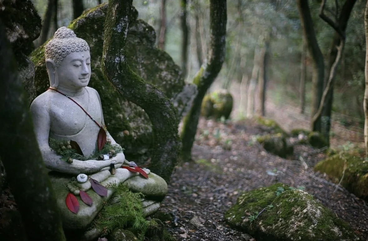 A woman sitting on a rocky ledge beside clear turquoise water with steep limestone cliffs in the background.
