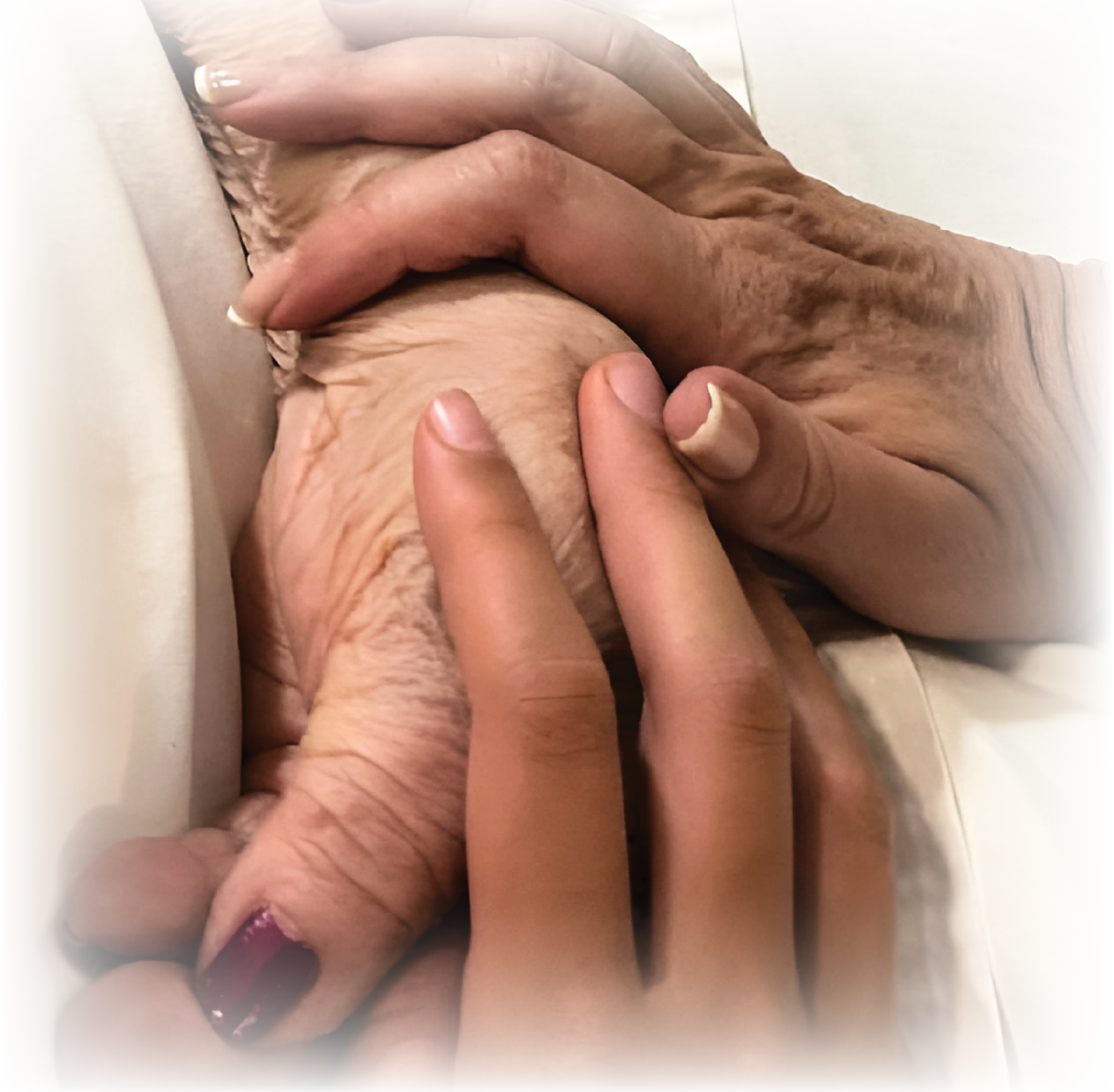 Close-up of a person's hand holding an older person's hand, both resting on a bed or pillow.