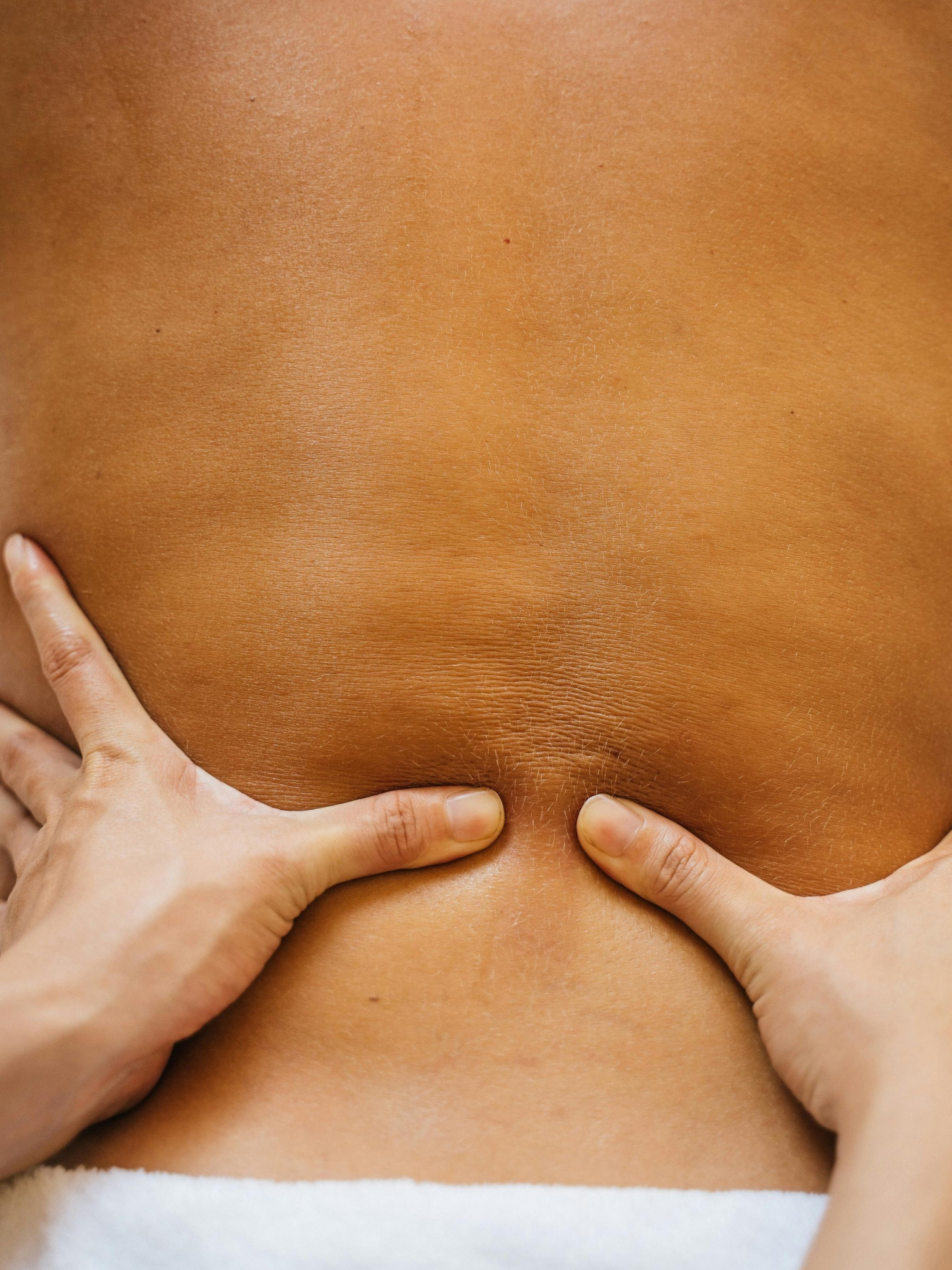 Close-up of a person's back with hands pressing on the lower back and side, showing smooth, tan skin.
