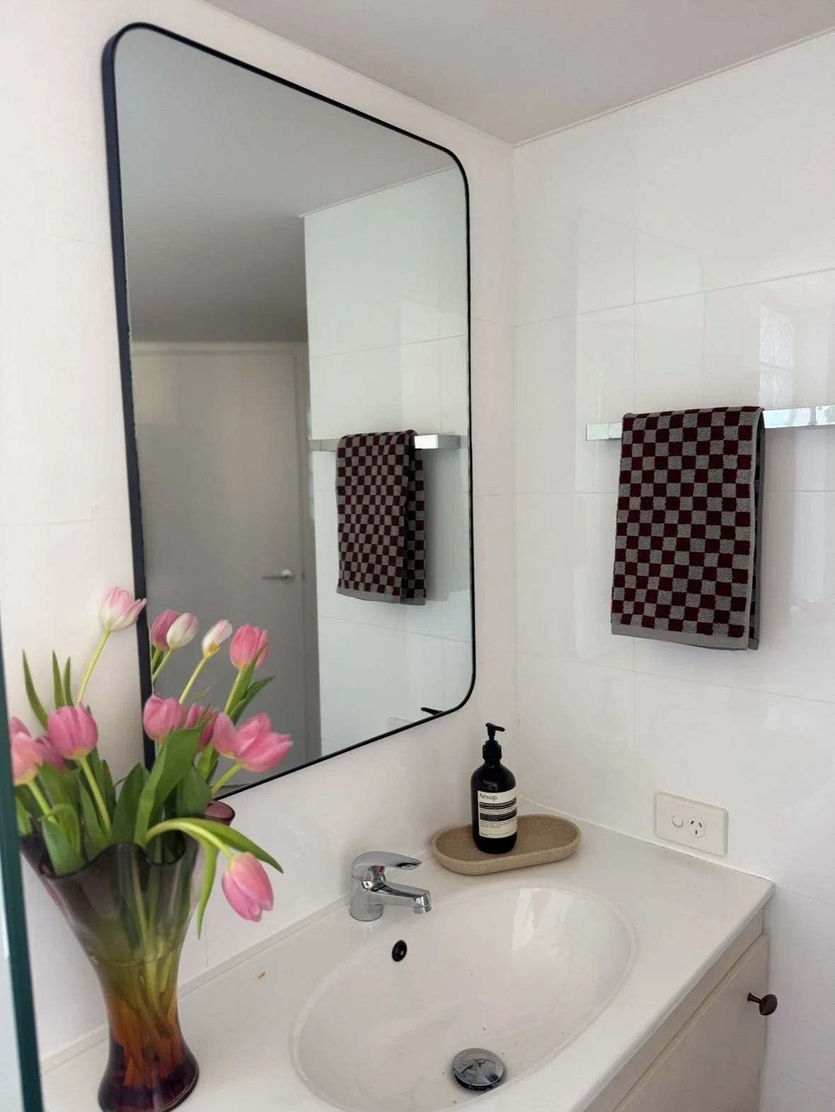White bathroom vanity with a vintage vase with pink tulips, dish-soap and high quality hand towel.
