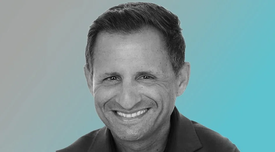 Black and white headshot of a smiling man with short dark hair against a gradient background.