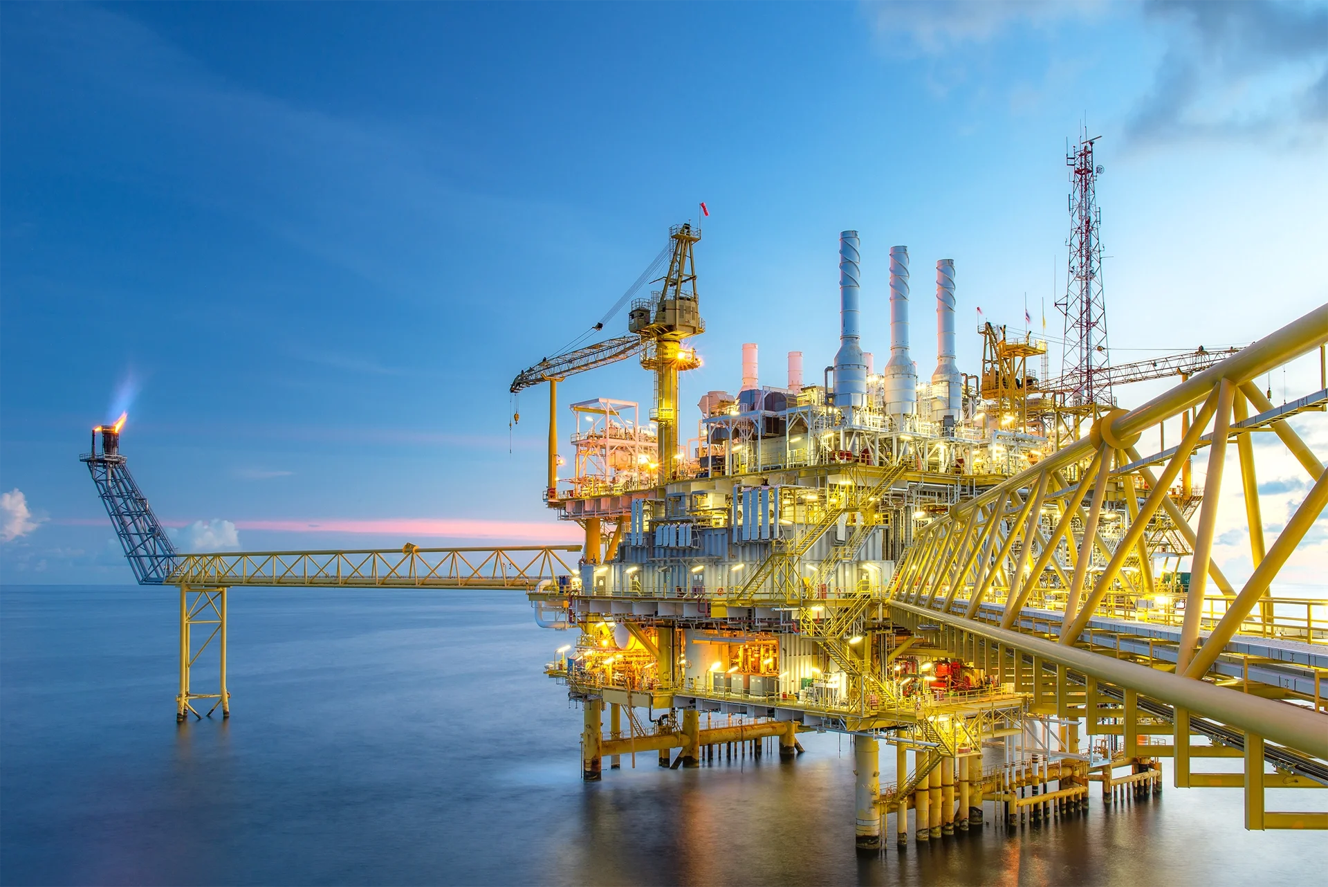 Offshore oil rig at sunset with blue sky and calm ocean water.