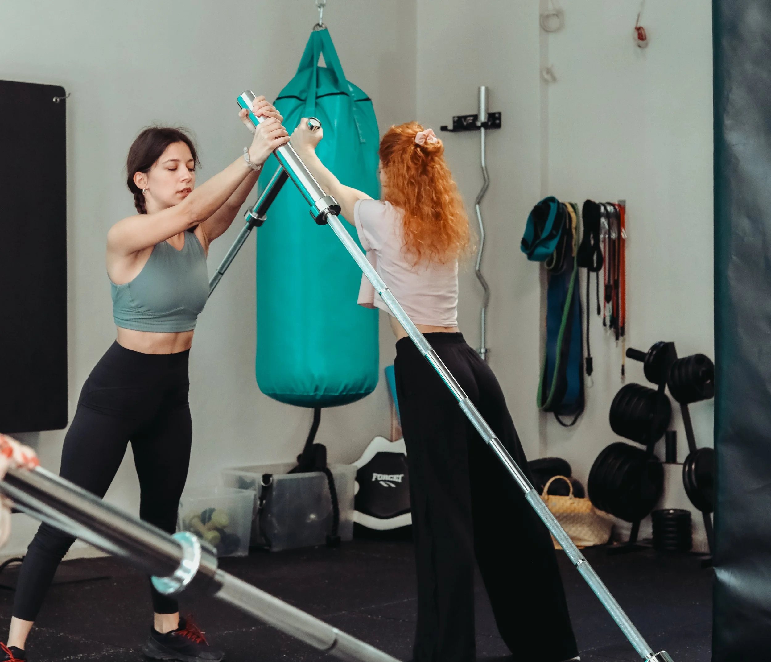 A person doing a kneeling cable and dumbbell exercise in a gym, with a punching bag, kettlebell, and neon sign in the background.
