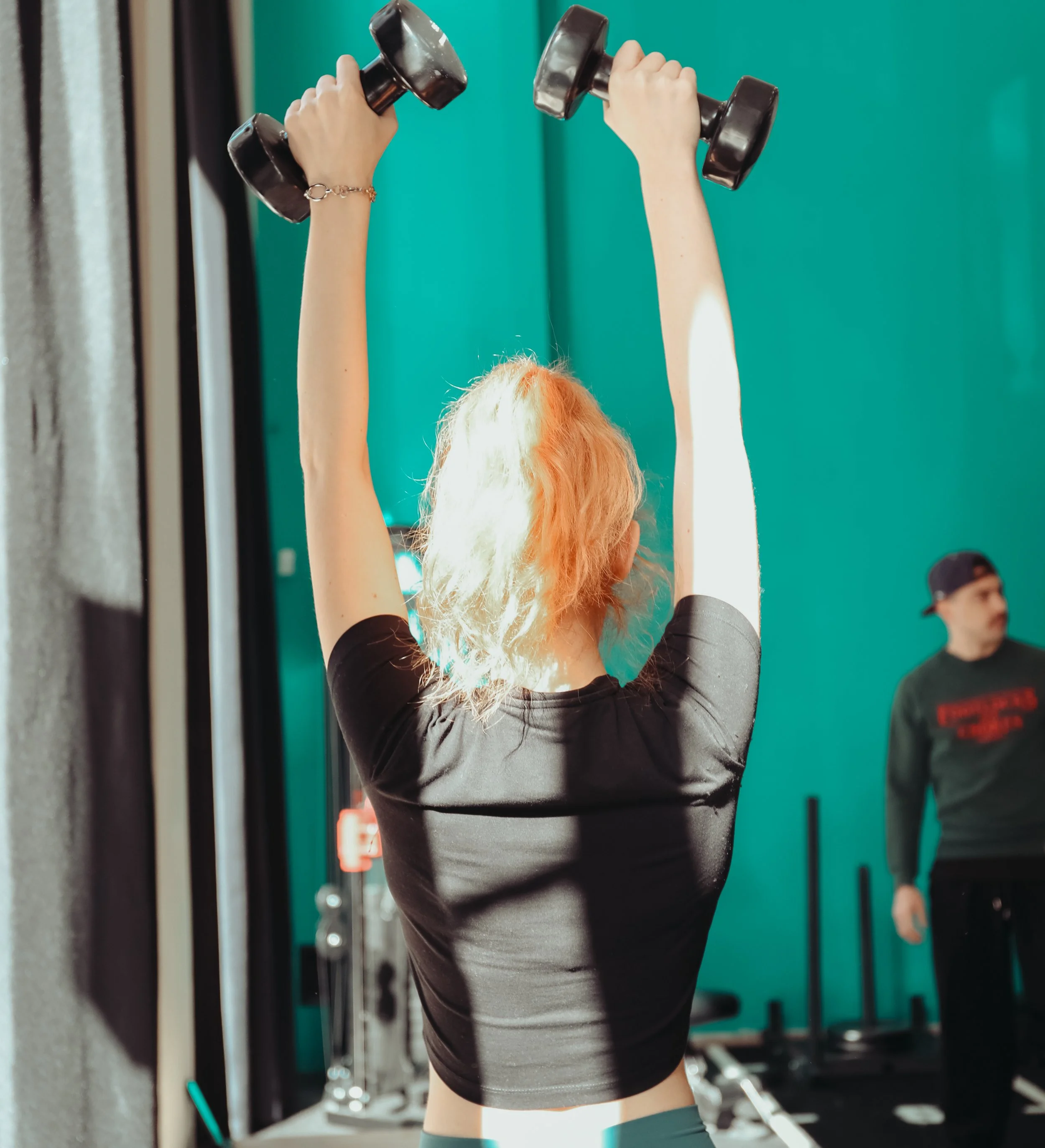 Woman in black workout clothes pushing weighted sled in gym with teal walls.