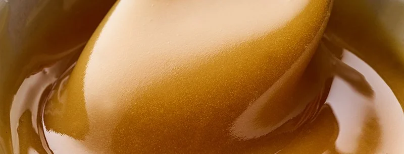 Close-up of a spoon dipped in smooth, melted caramel sauce.