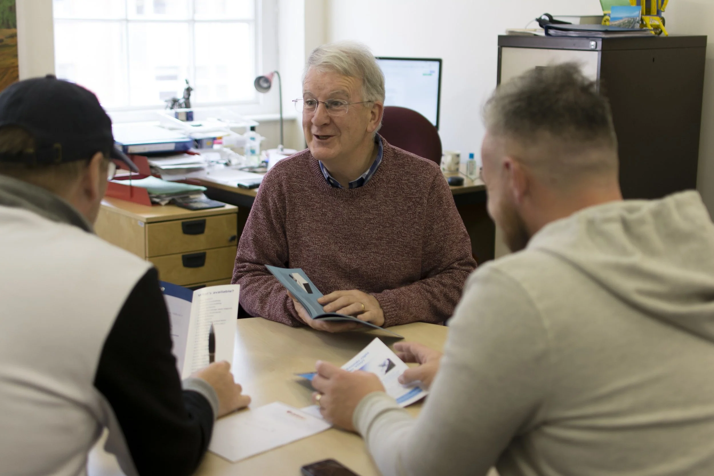 Two people sitting at a desk, reviewing documents, with one person pointing at papers and the other holding a pen.