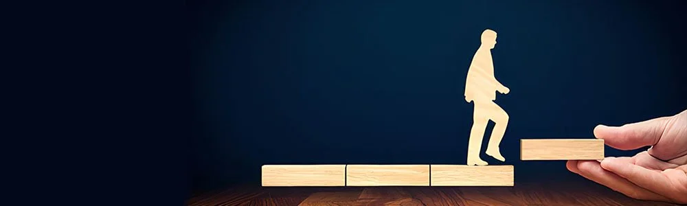 Silhouettes of four people helping each other climb a hill during sunset.